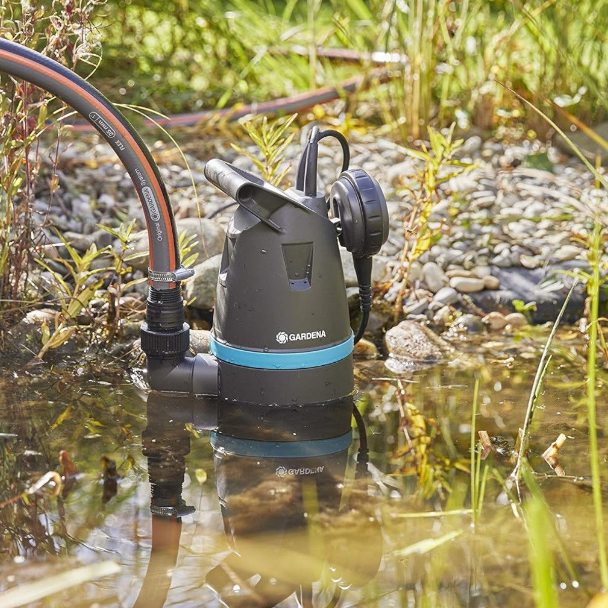 Pompa sommersa nera con fascia blu in stagno, tubo collegato.