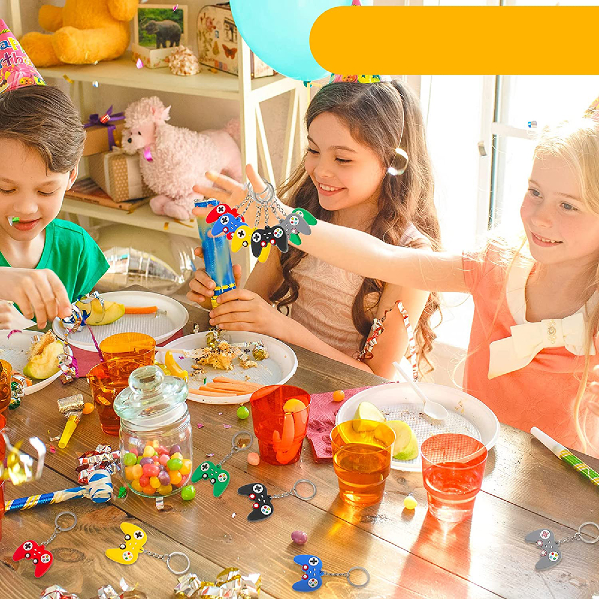 Kinder feiern Geburtstag, spielen mit Schlüsselanhängern in Form von Controllern. Süßigkeiten und Kuchen sind auf dem Tisch.