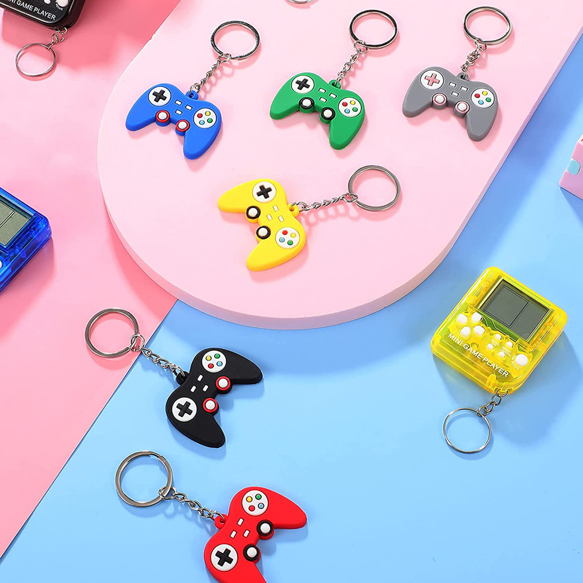 Bunte Gamecontroller-Schlüsselanhänger und Mini-Spieler auf rosa-blauem Hintergrund.