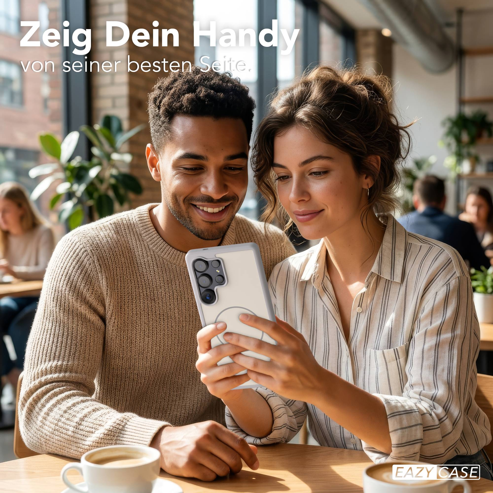 Ein Mann und eine Frau schauen auf ein Handy. Kaffeetassen stehen auf dem Tisch.