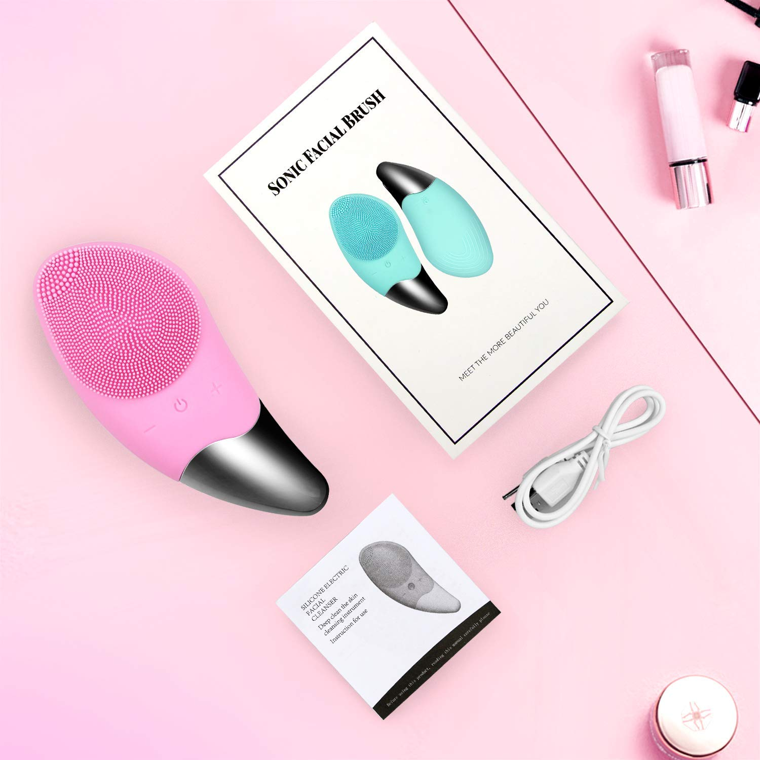 Rosa Schall-Gesichtsreinigungsbürste, Handbuch, Ladekabel und Make-up-Artikel auf rosa Hintergrund.