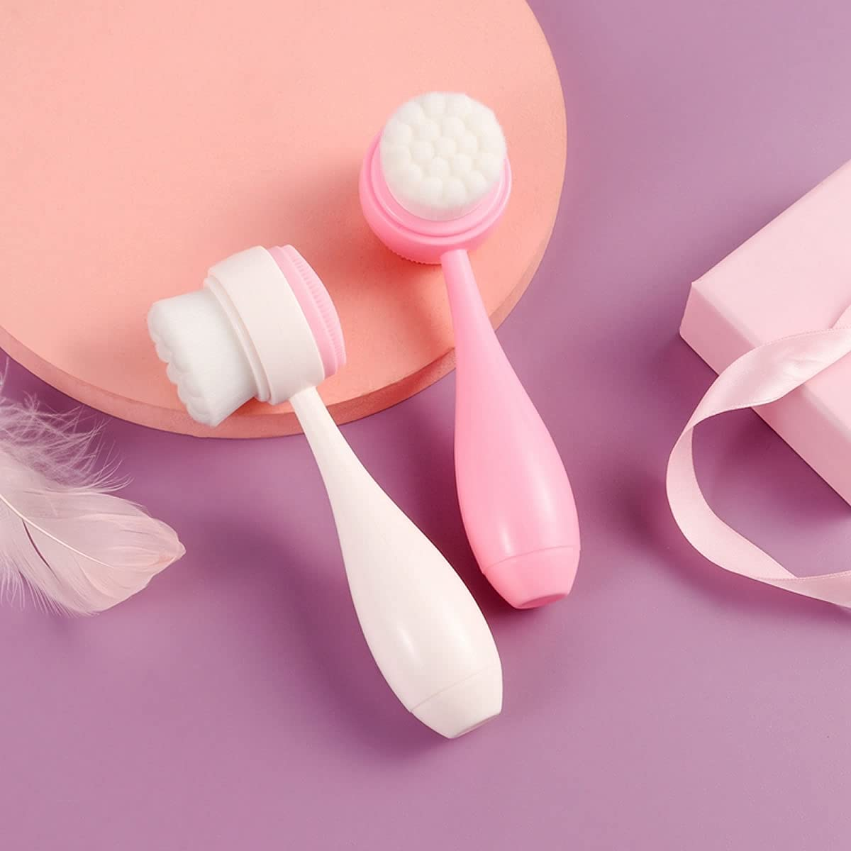 Zwei Gesichtsreinigungspinsel, einer weiß, einer pink, auf lila und rosa Untergrund.