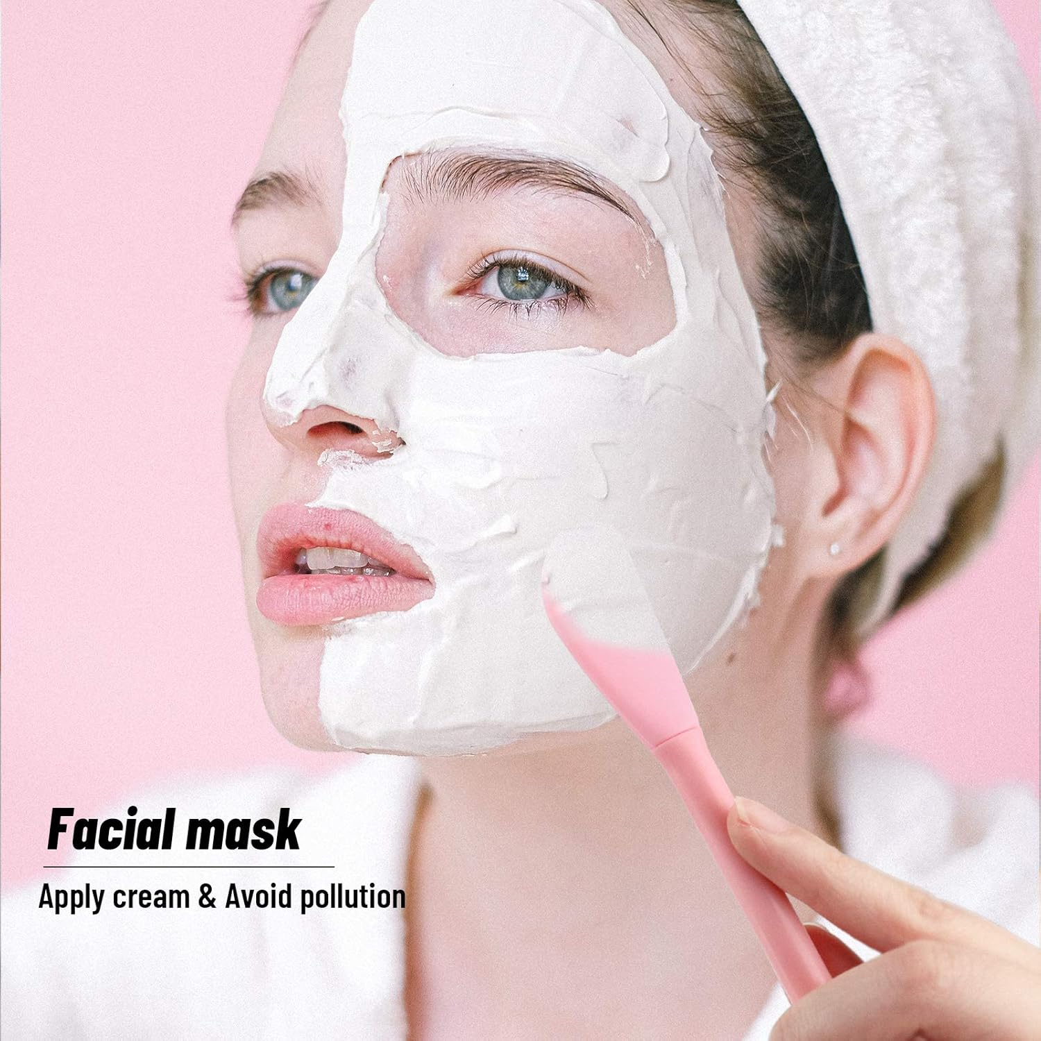 Eine Frau mit einer weißen Gesichtsmaske und einem rosa Pinsel auf rosafarbenem Hintergrund.