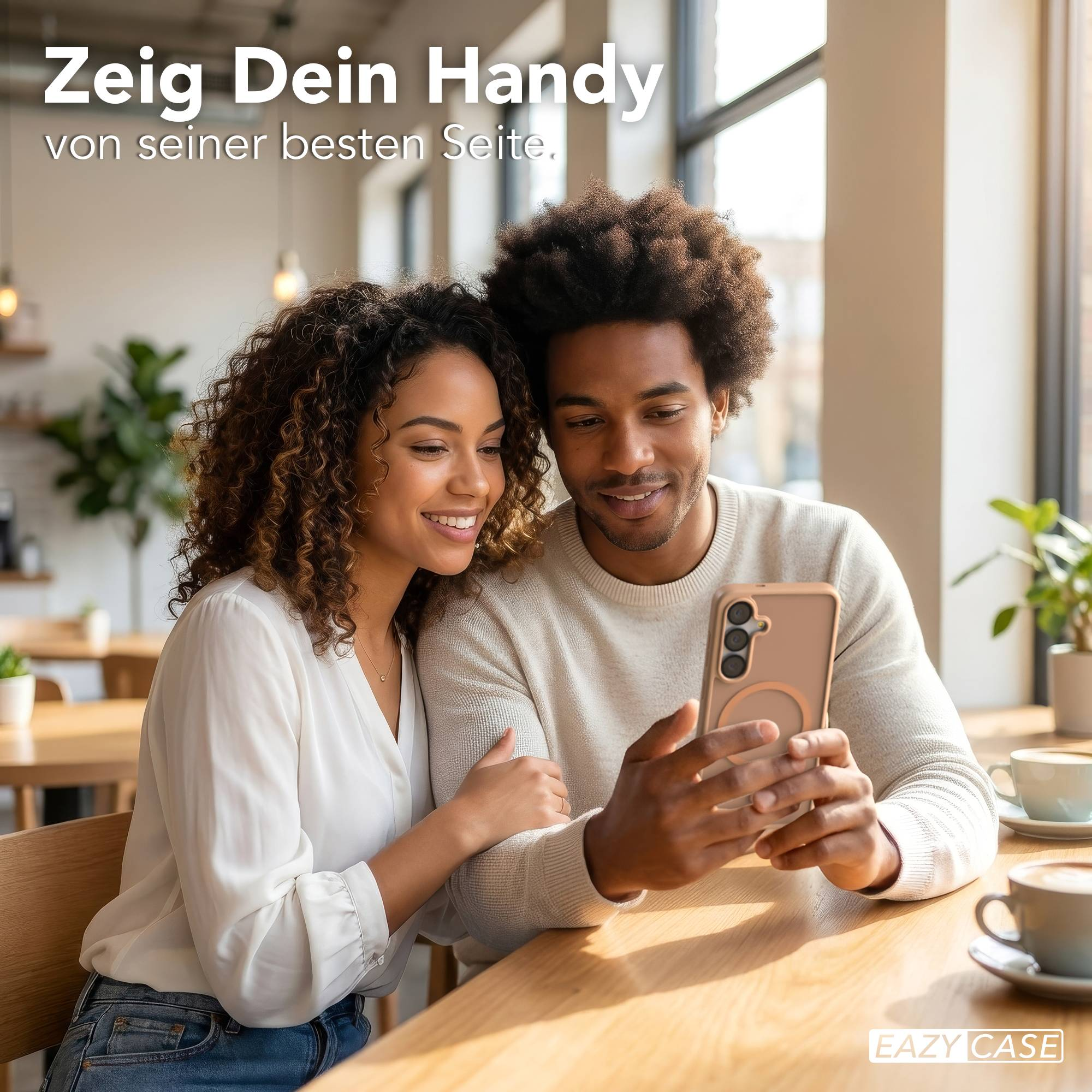 Ein Paar schaut auf ein Handy, das der Mann hält. Im Hintergrund sind Tische und Pflanzen.