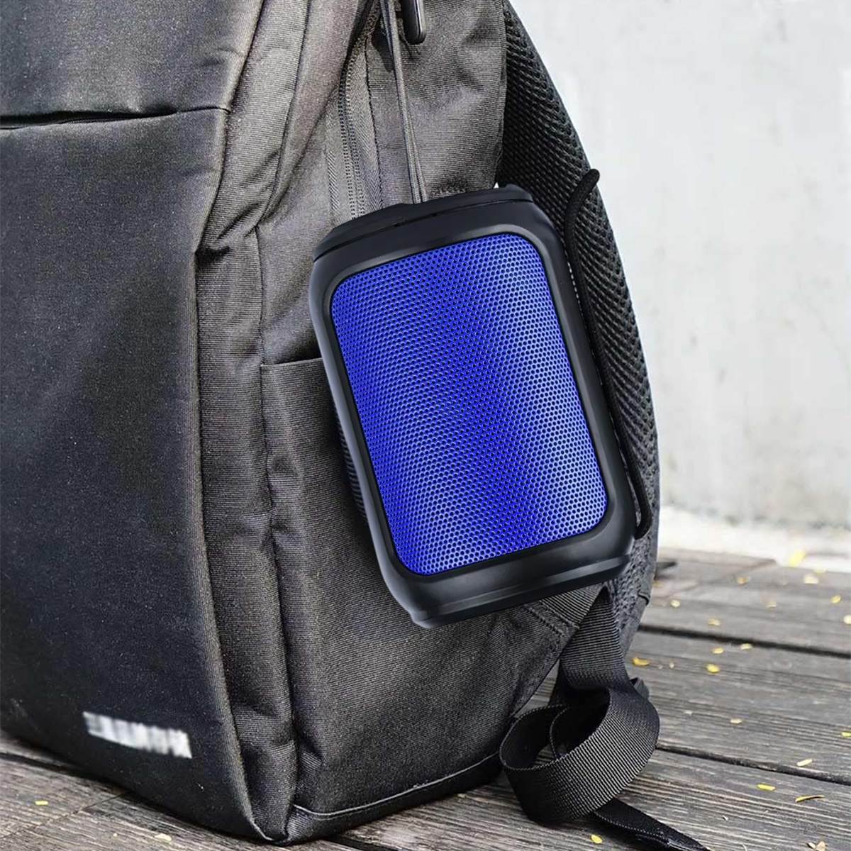 Ein blauer Lautsprecher hängt an einem schwarzen Rucksack auf Holzdielen.
