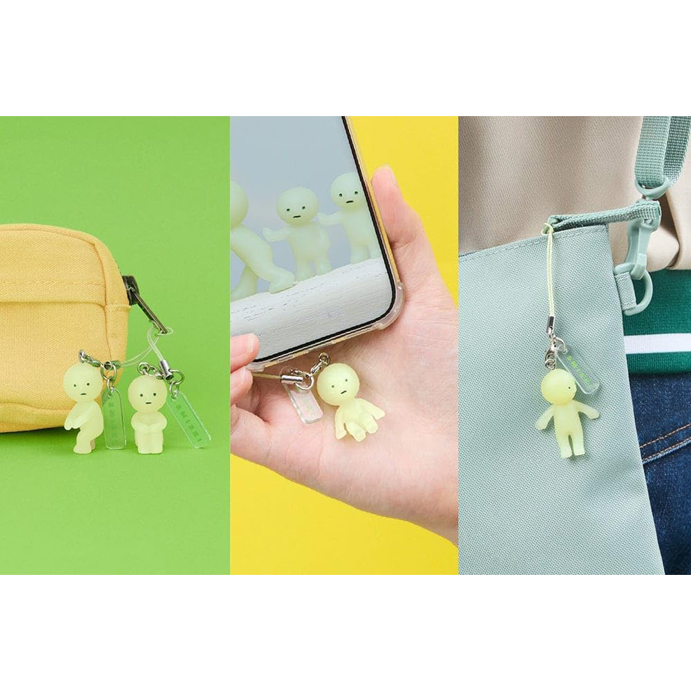 Drei kleine gelbe Figuren mit Schnüren, befestigt an einer Tasche und einem Handy.