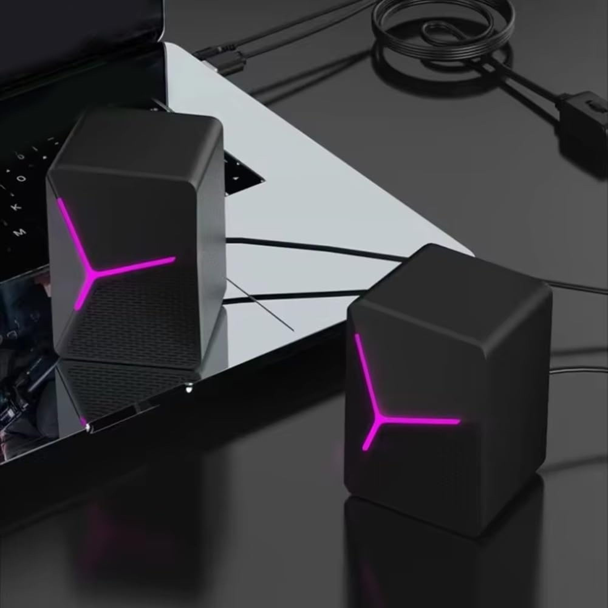 Zwei schwarze Würfel-Lautsprecher mit pink leuchtenden Akzenten sitzen auf einem Laptop.