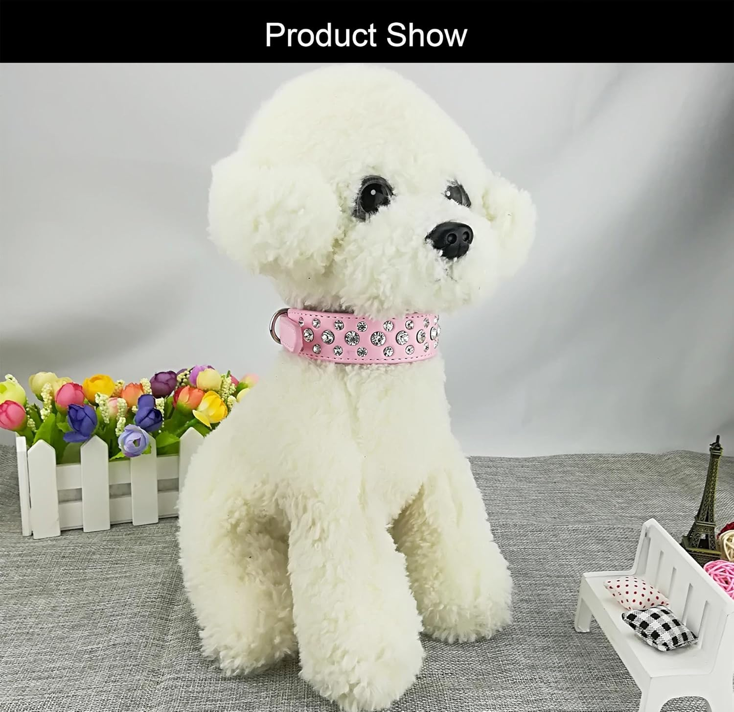 Ein weißer Plüschhund mit rosa Halsband sitzt vor Blumen und einer Bank.
