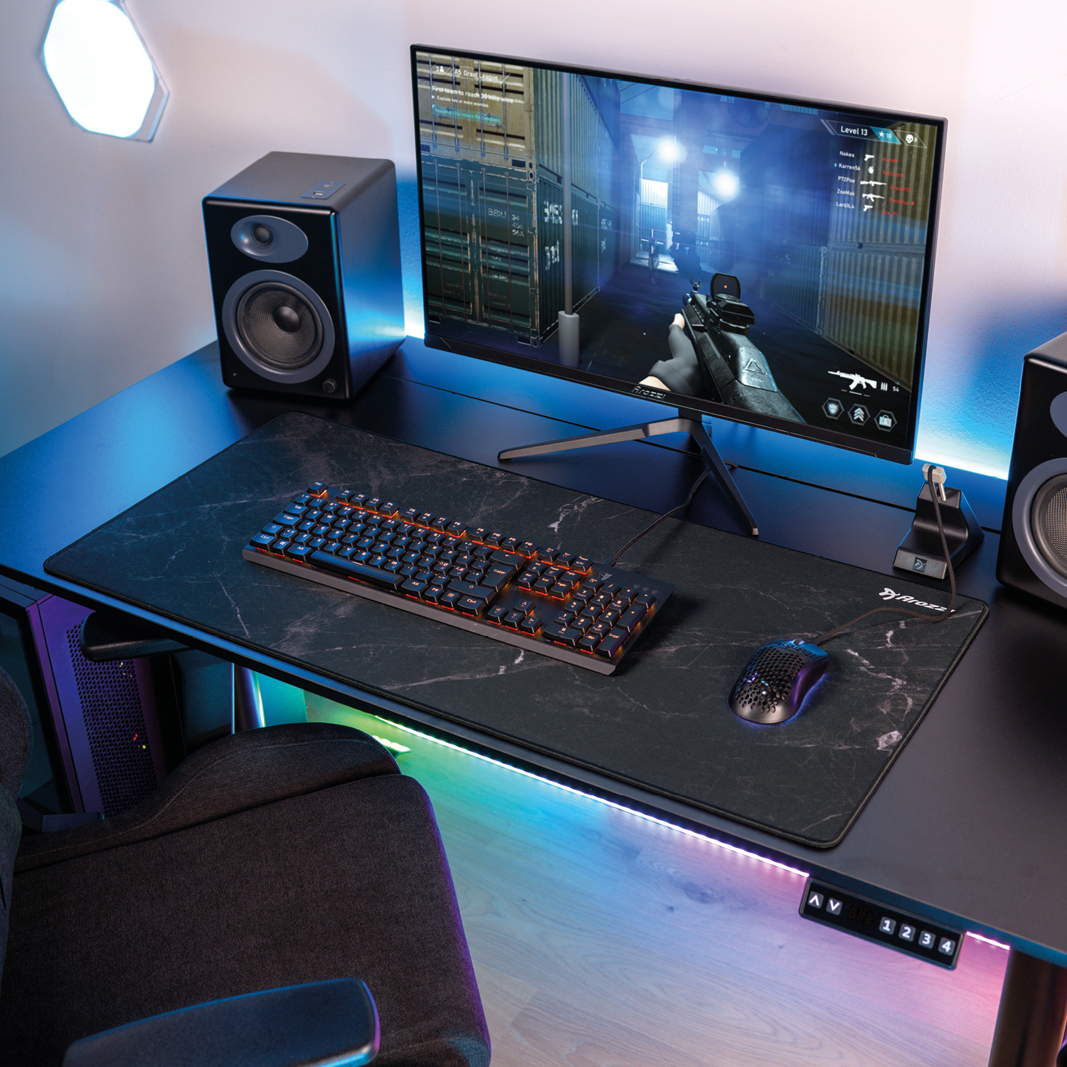 Ein Gaming-Setup mit einem Monitor, der ein Ego-Shooter-Spiel anzeigt, Tastatur, Maus, Lautsprecher und Stuhl.