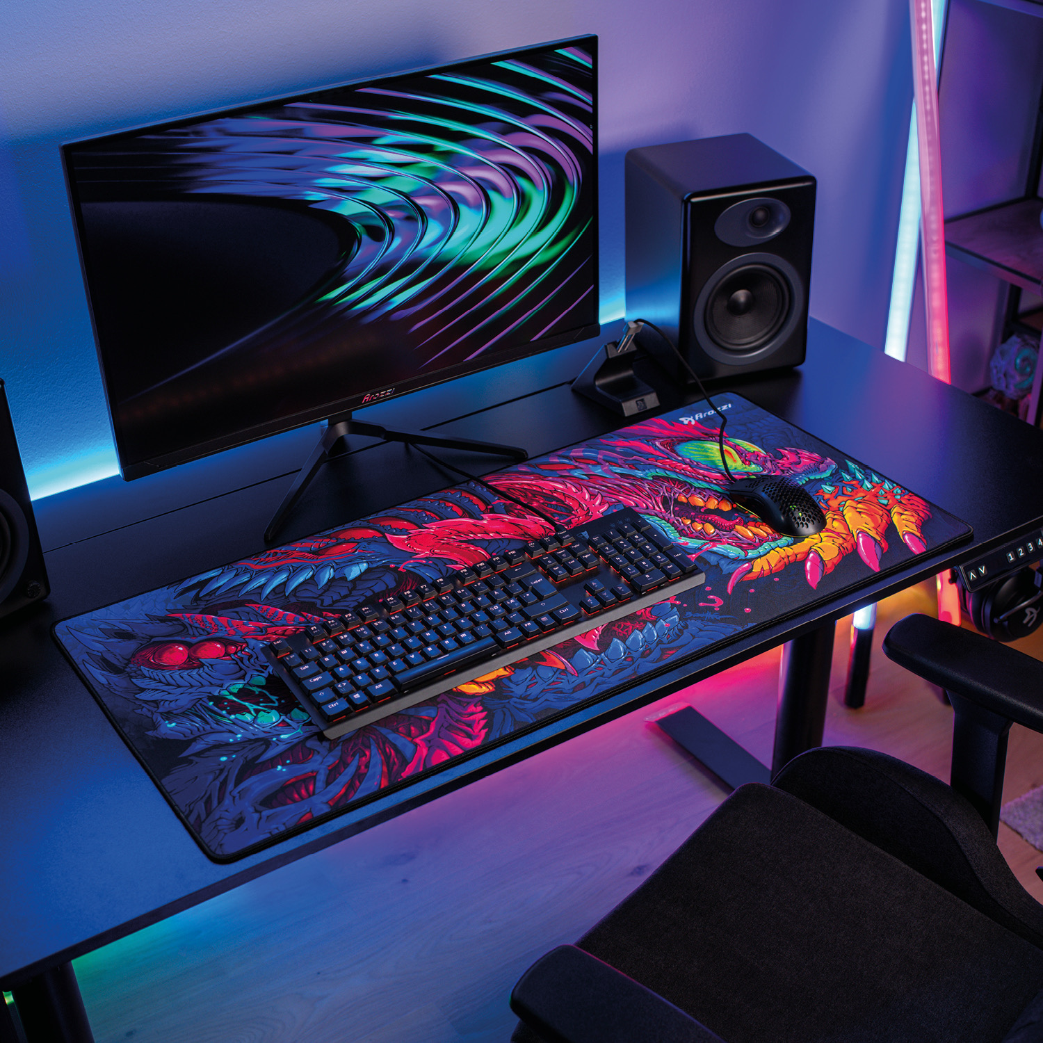 Ein Gaming-Schreibtisch mit Monitor, Tastatur, Maus und buntem Mauspads mit Drachenmotiv.