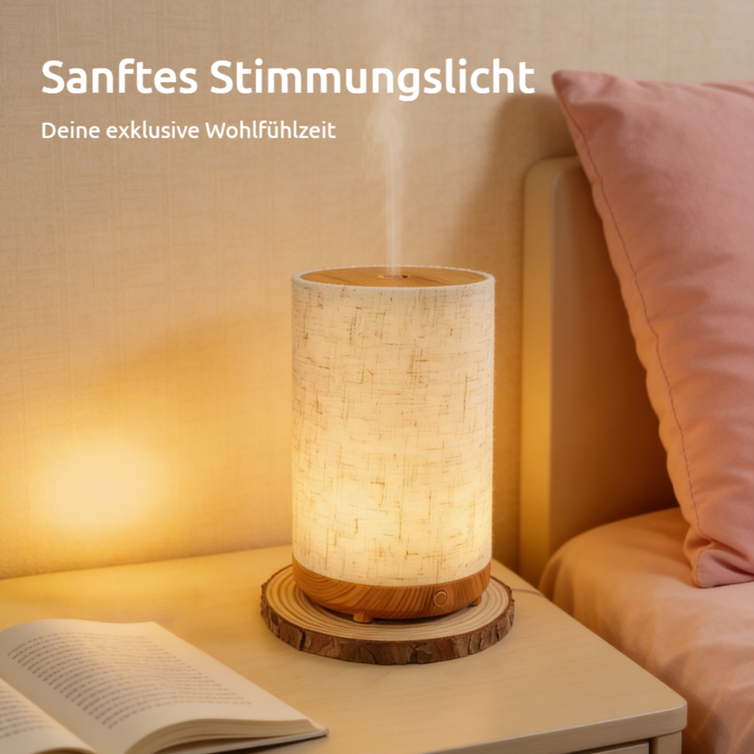 Ein Nachttisch beherbergt einen beleuchteten Diffusor mit Stoffschirm, neben einem offenen Buch und einem rosa Kissen.