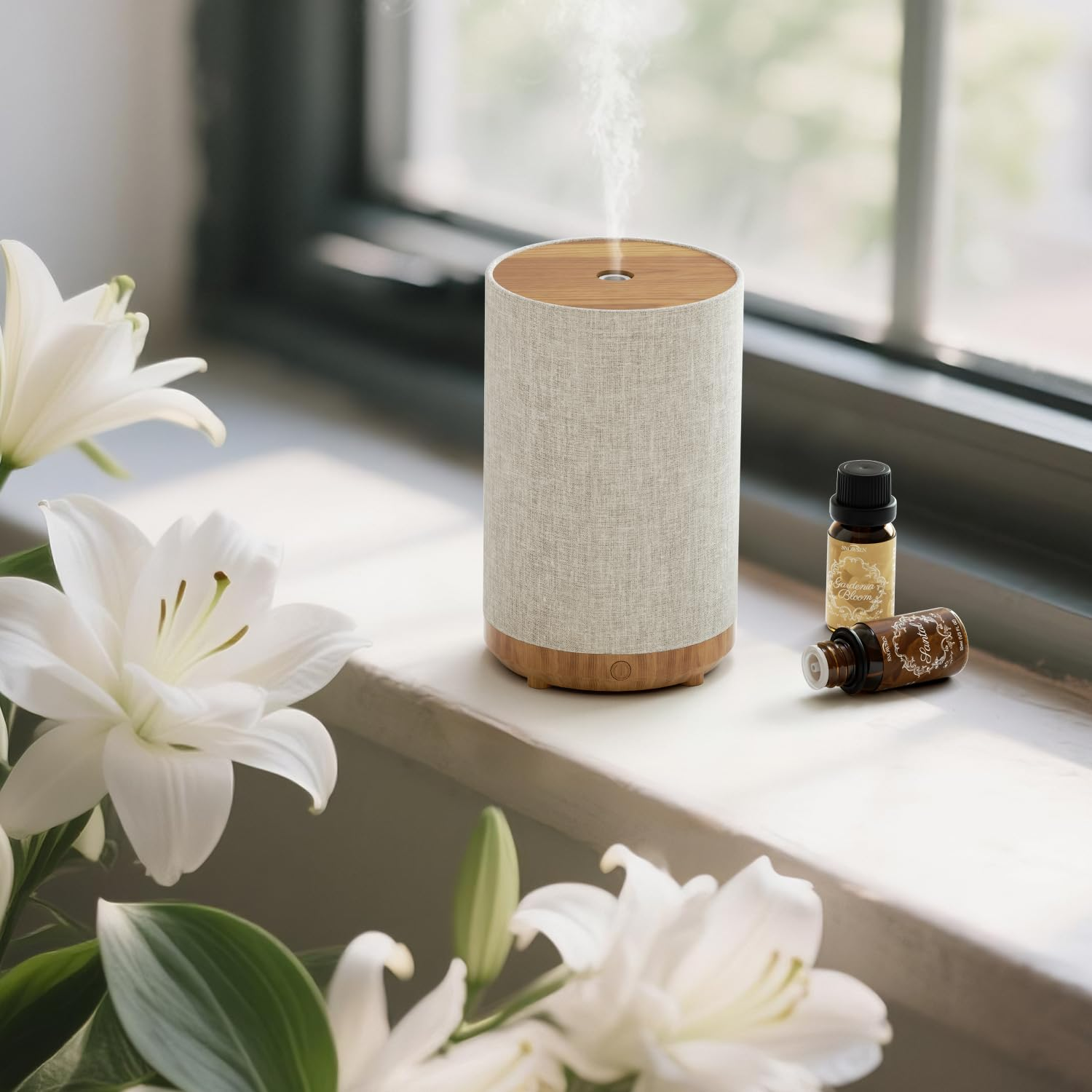 Aromatherapie-Diffusor mit ätherischen Ölflaschen und weißen Lilien auf einem Fensterbrett.