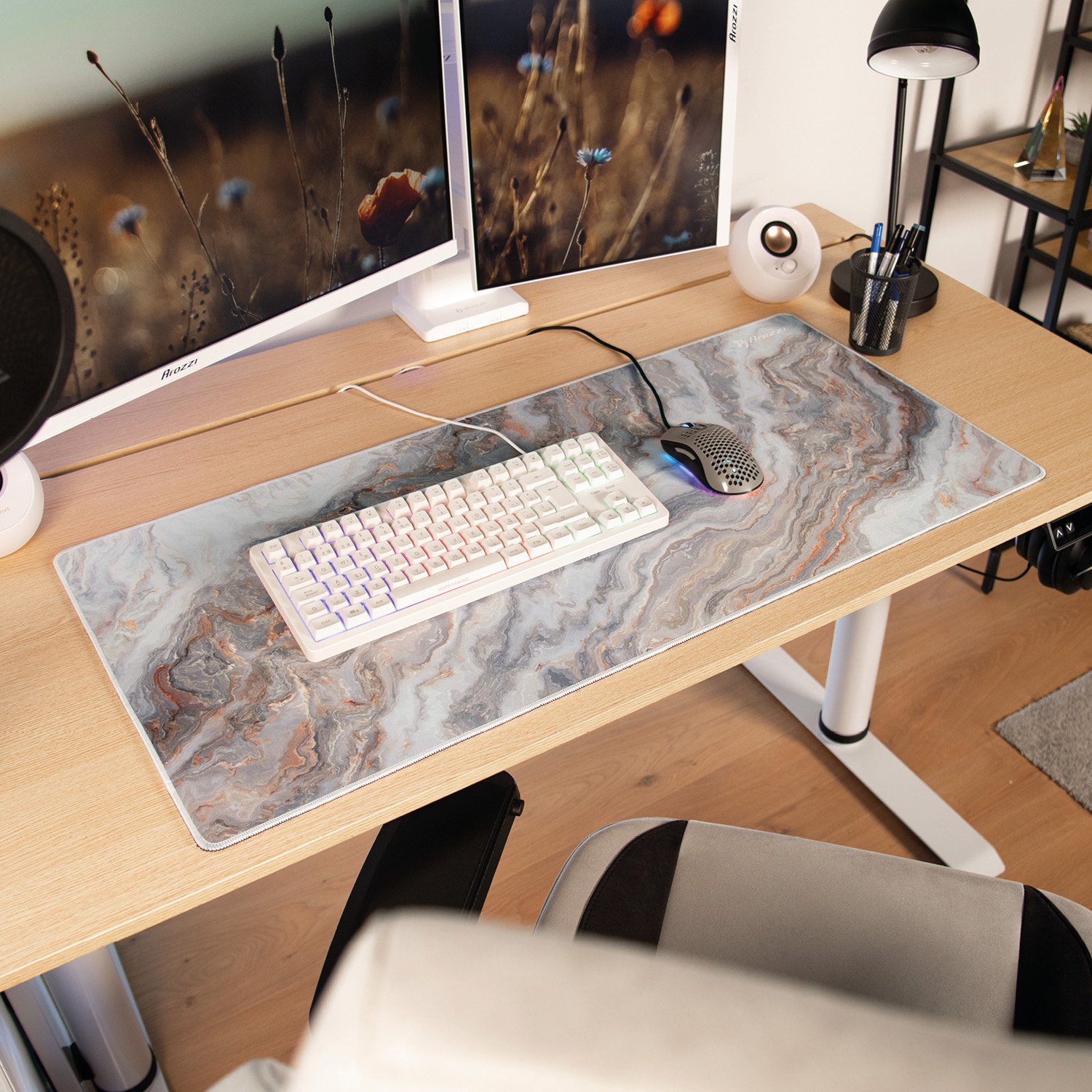 Eine weiße Tastatur und Maus auf einer Marmor-Schreibtischunterlage, mit zwei Monitoren, die Naturszenen zeigen.