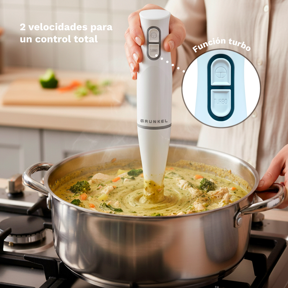 Batidora de mano blanca mezcla sopa verde en olla sobre la estufa.