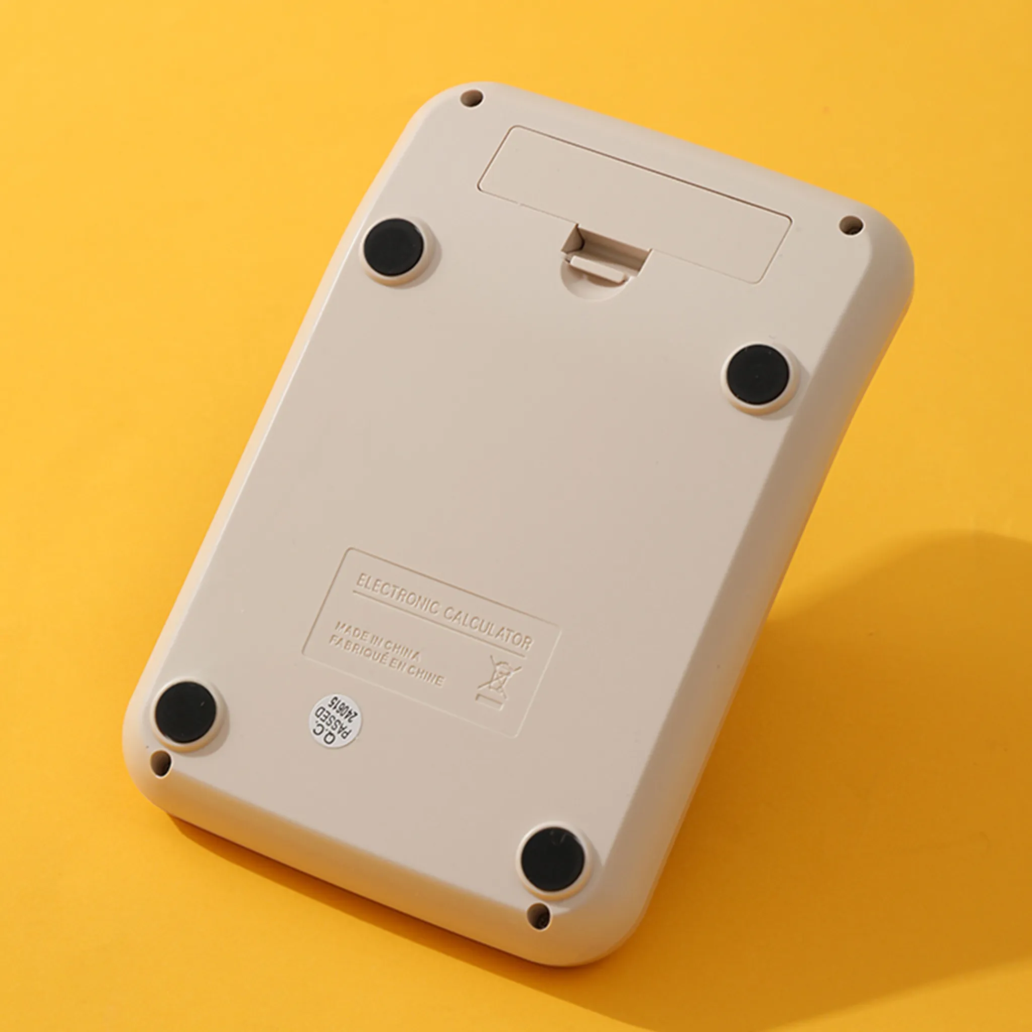 Die Unterseite eines beigefarbenen elektronischen Taschenrechners mit vier Gummifüßen auf gelbem Hintergrund.