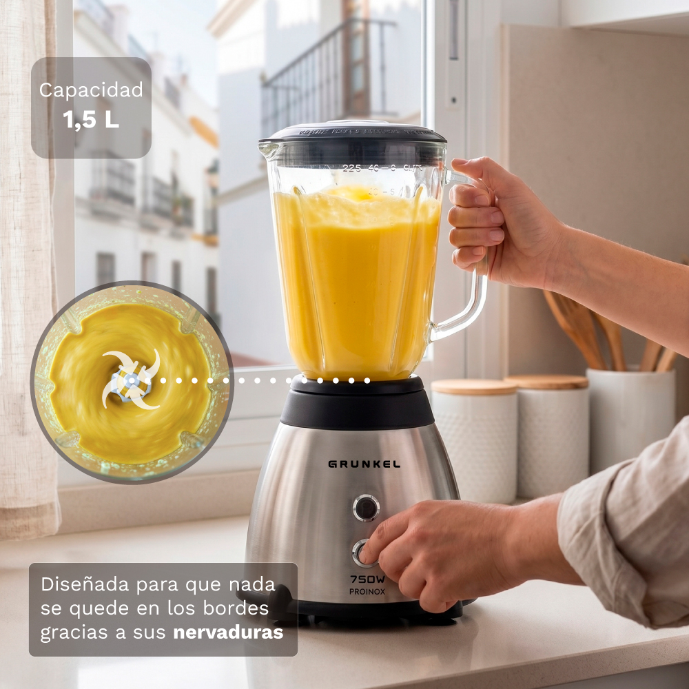 Una licuadora plateada con un vaso de vidrio lleno de líquido amarillo es operada por una mano.