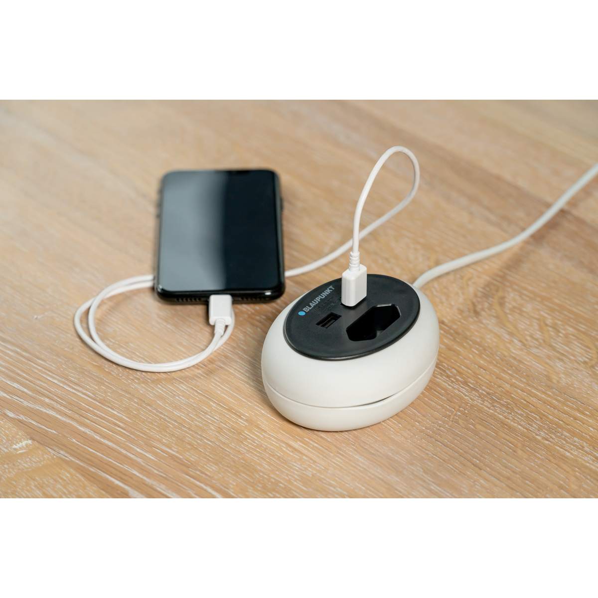 Ein Smartphone wird über ein weißes USB-Kabel an einen weißen Reiseadapter angeschlossen.