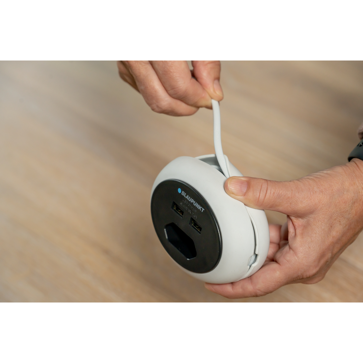 Eine Hand hält ein weißes Ladegerät mit USB-Anschlüssen und einer Steckdose.