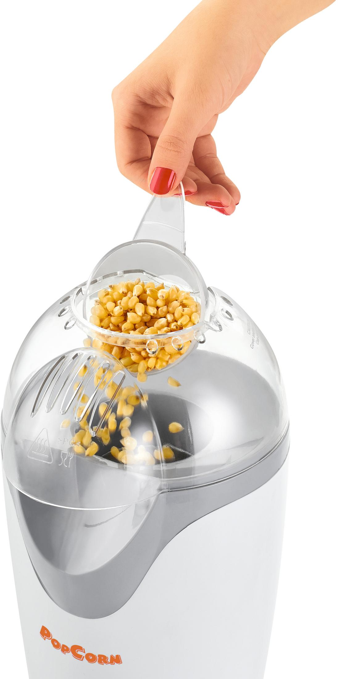 Eine Hand mit roten Nägeln schüttet Maiskörner in einen Popcornmacher.