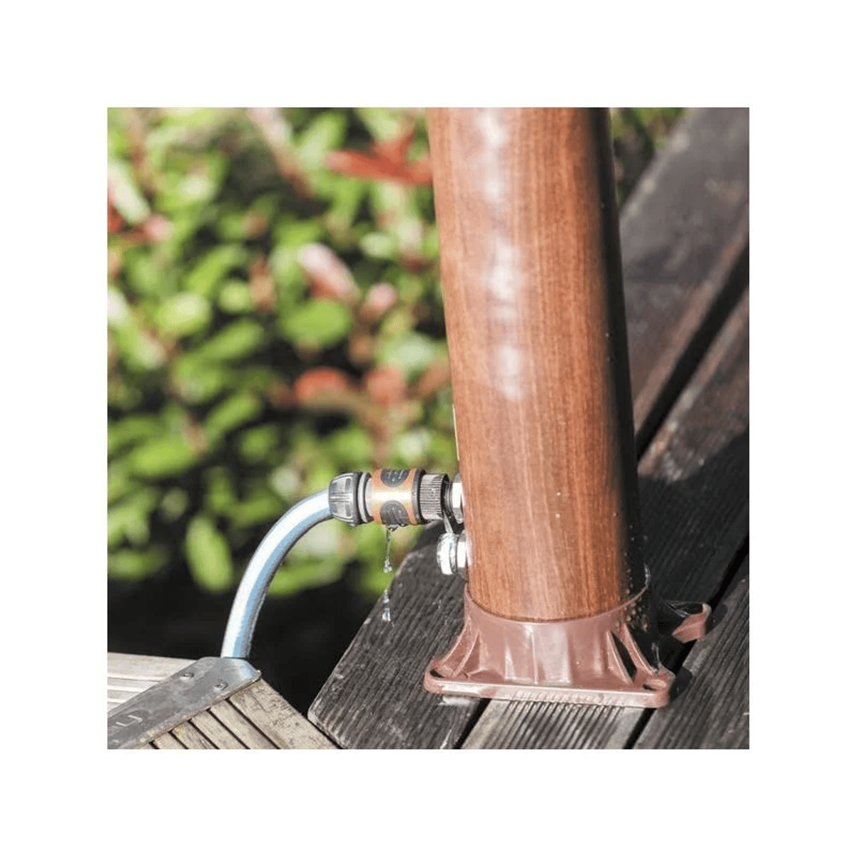 Un conector de manguera gotea agua sobre una superficie de madera junto a un poste.