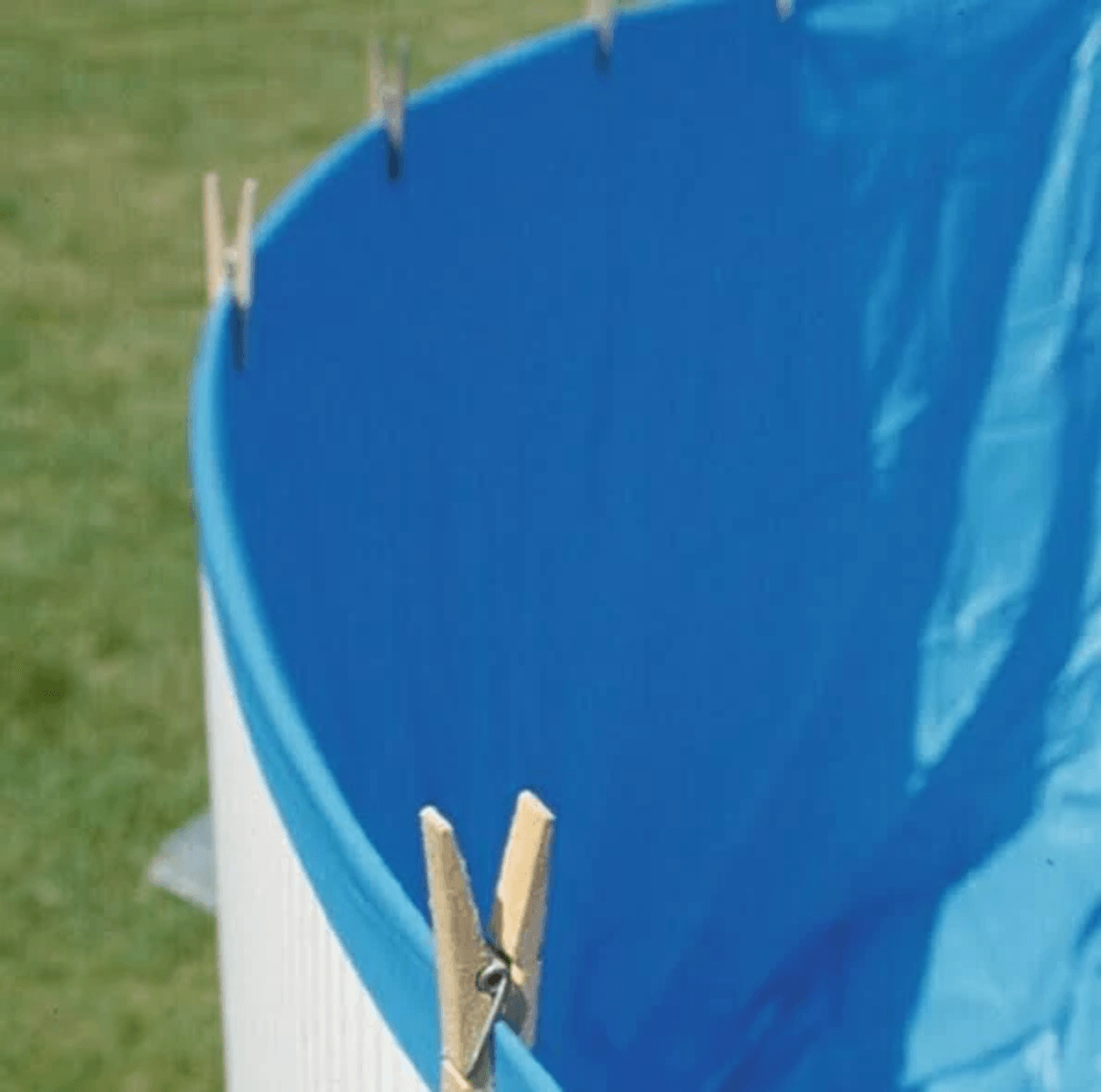 Una piscina redonda y blanca con revestimiento azul, sobre césped. Pinzas de ropa de madera sujetan el borde.