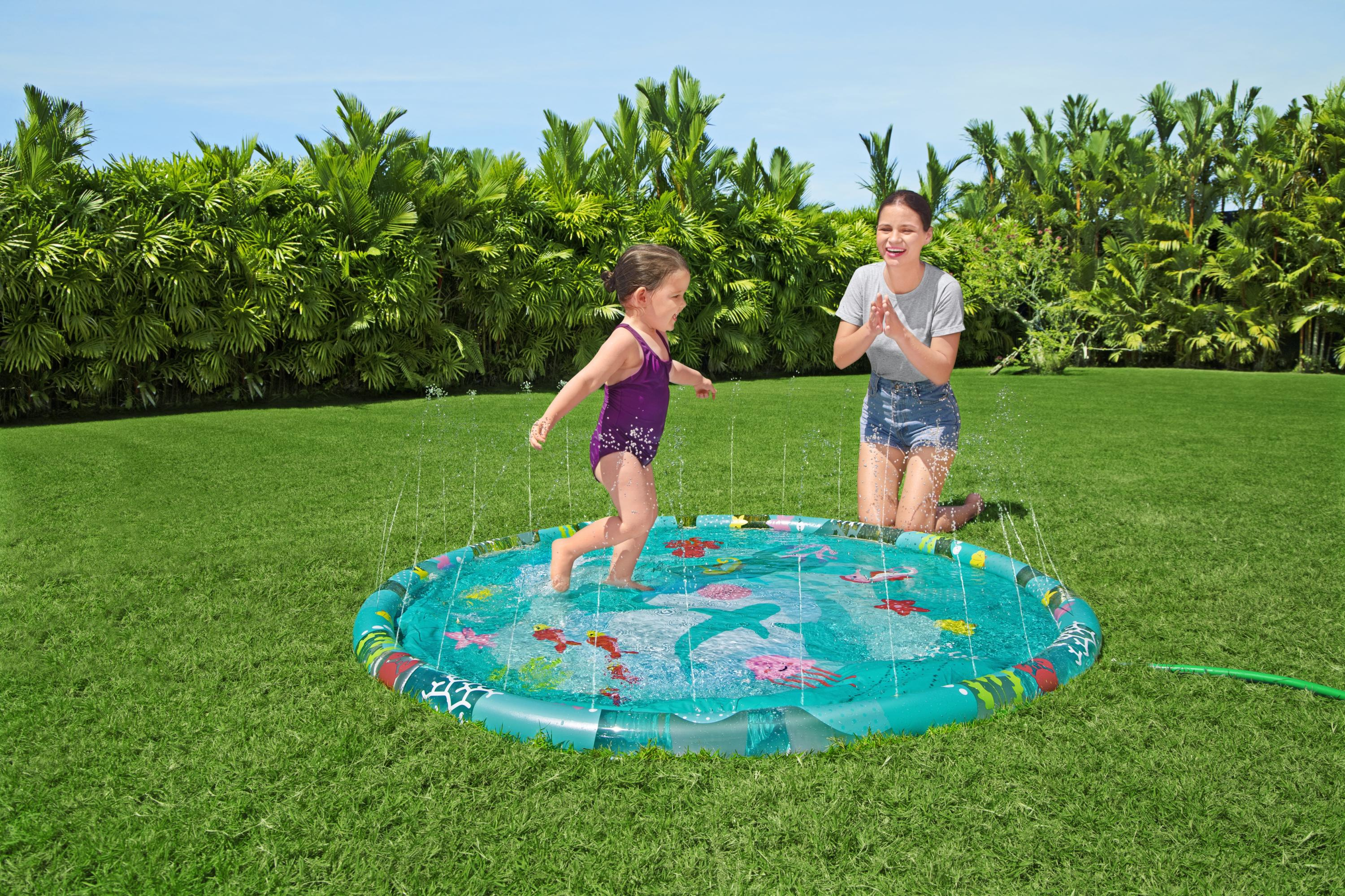 Madre e hija juegan en una piscina inflable sobre césped verde con palmeras.