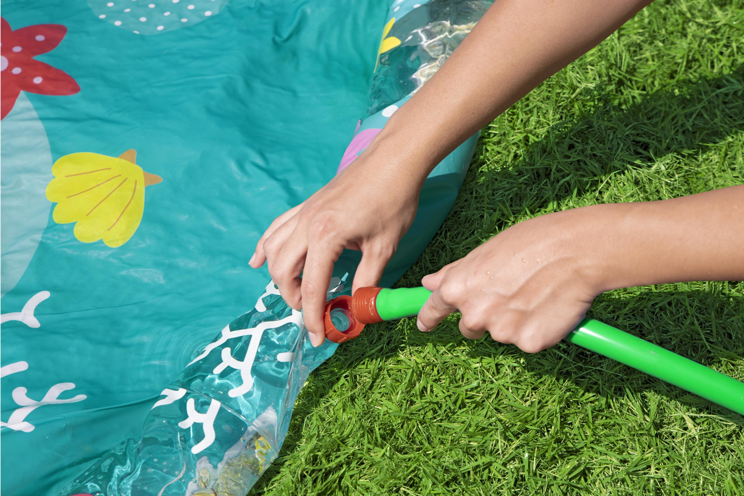 Manos conectan manguera verde con conector rojo a piscina inflable sobre césped.