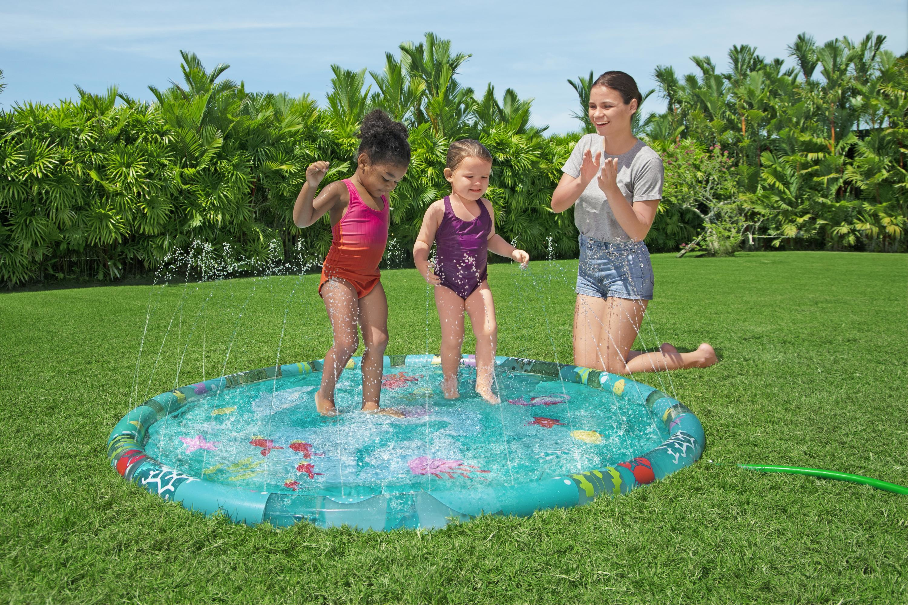 Dos niñas chapotean en una piscina inflable mientras una mujer las observa.