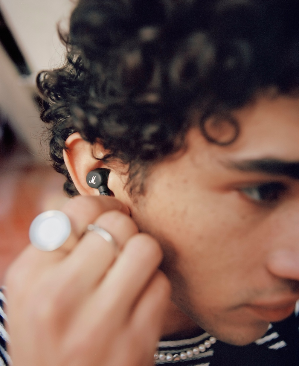 Un uomo con capelli ricci inserisce un auricolare nero con logo Marshall.
