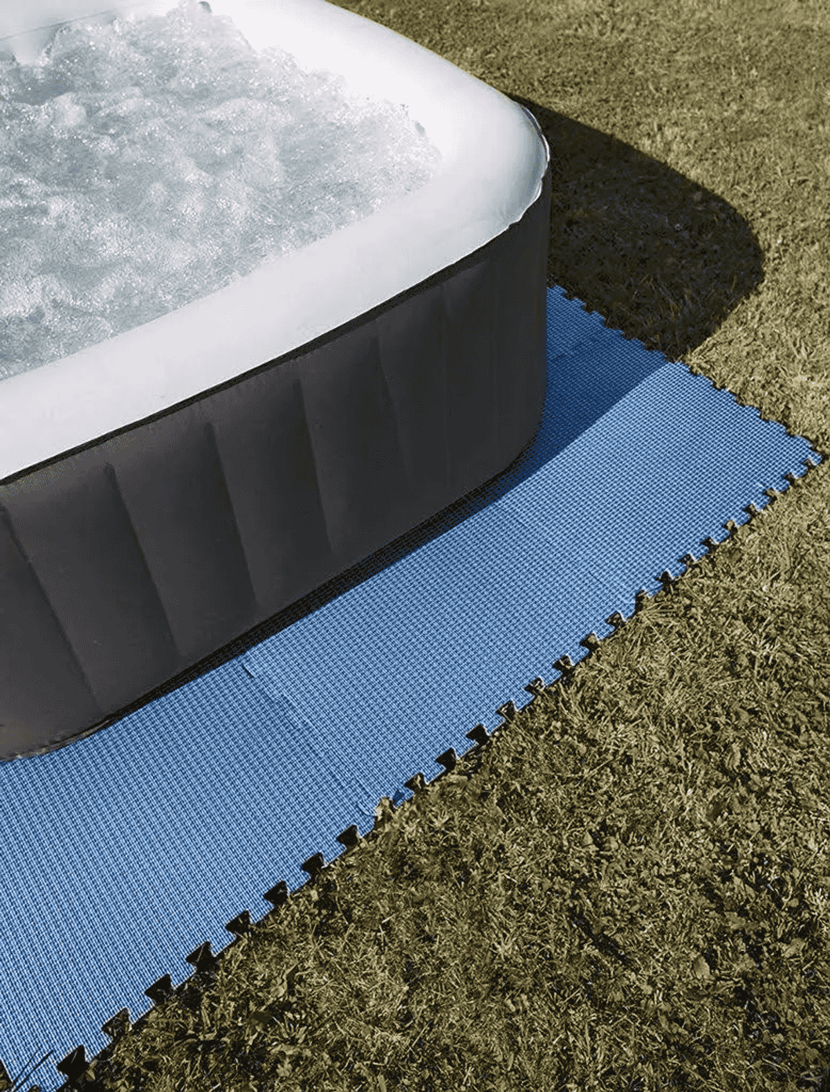 Jacuzzi inflable sobre alfombrilla azul en césped.