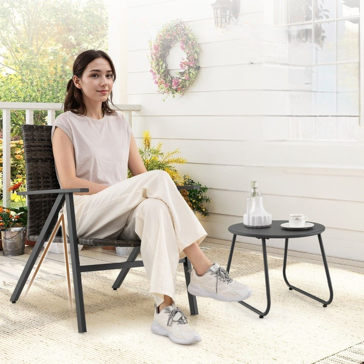 Vrouw zit op een stoel op een veranda met een tafel en een koffiekopje.