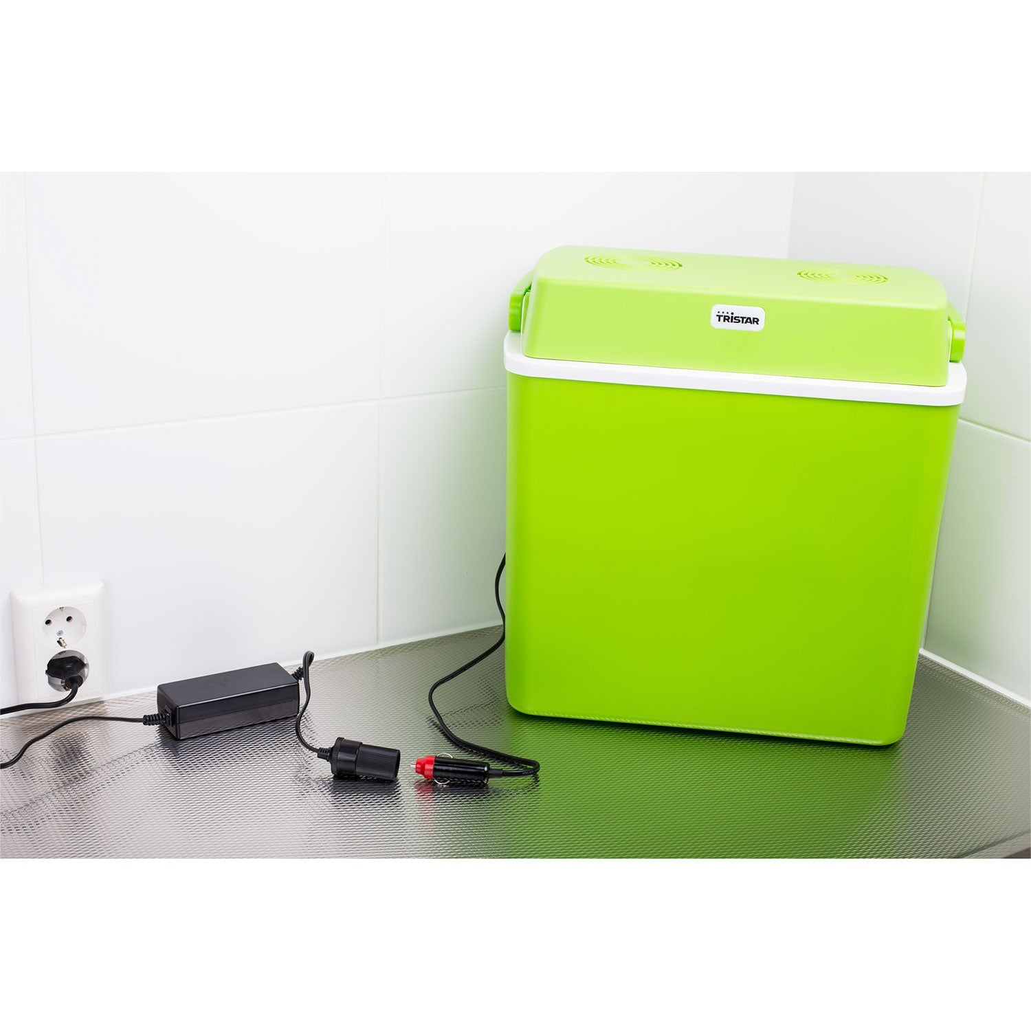 Een limoengroene koelbox met wit deksel staat op een aanrecht, aangesloten op een stroomadapter.