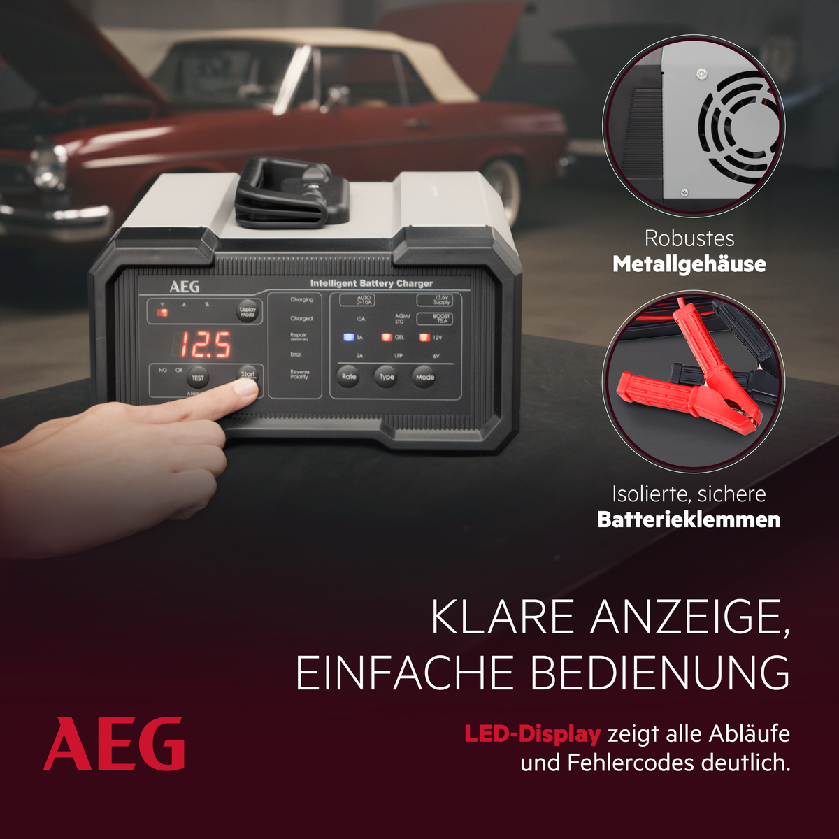 Intelligentes Ladegerät mit LED-Display und roten Klemmen vor altem Auto.