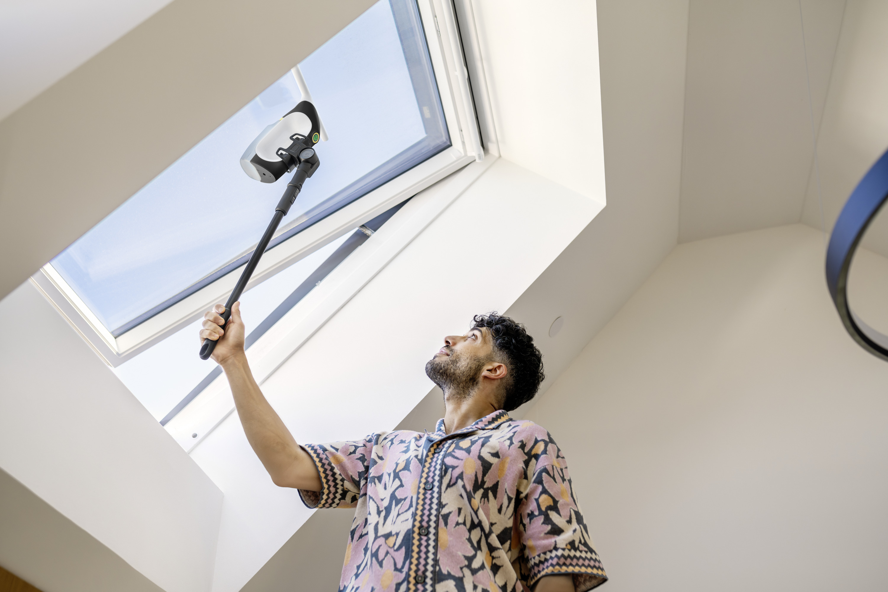 Ein Mann reinigt mit einem Fensterreinigungsgerät ein Dachfenster.