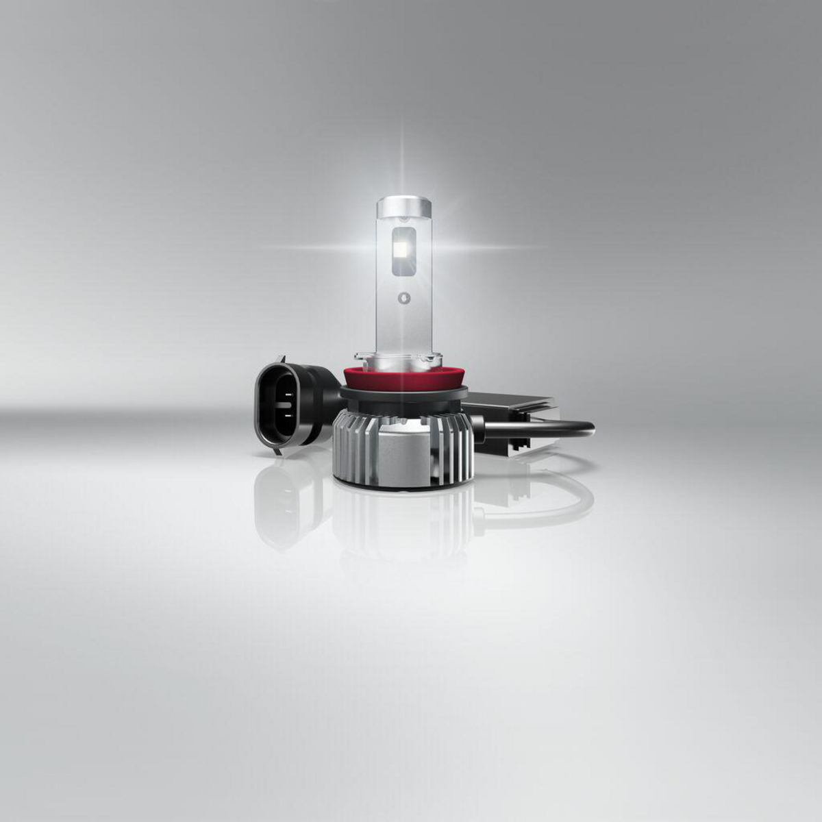 Eine LED-Autolampe mit silbernem Kühlkörper und rotem Ring, auf grauem Hintergrund.