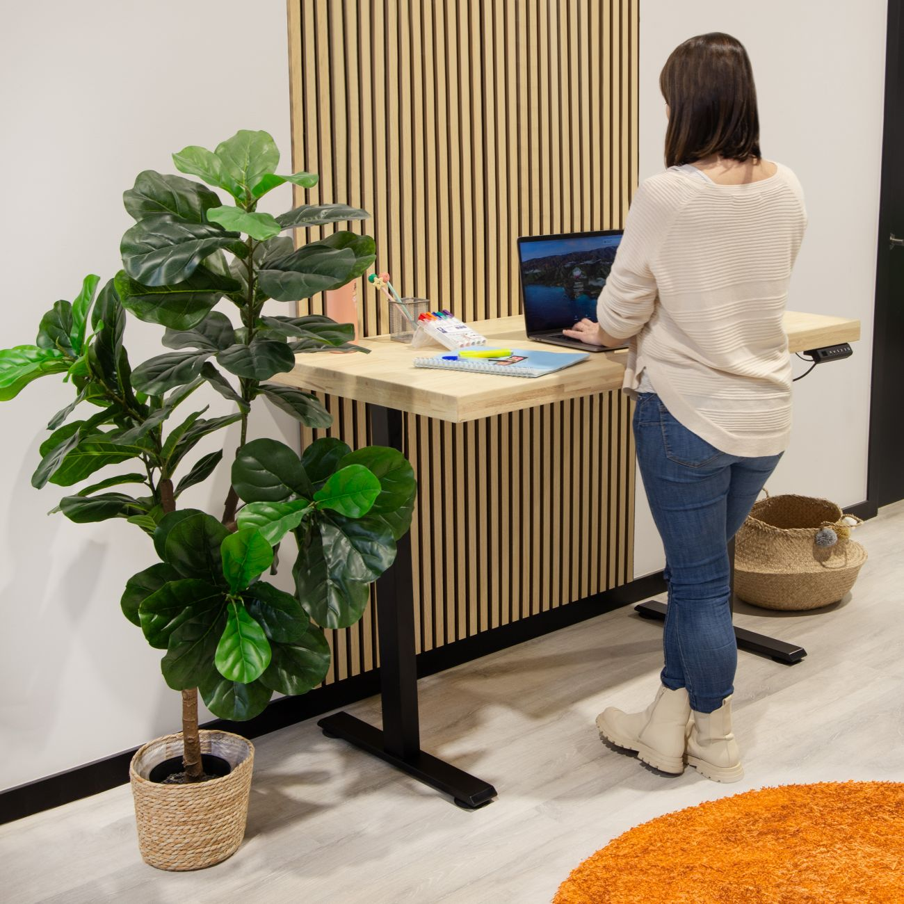 Una mujer está de pie en un escritorio ajustable con laptop y plantas.