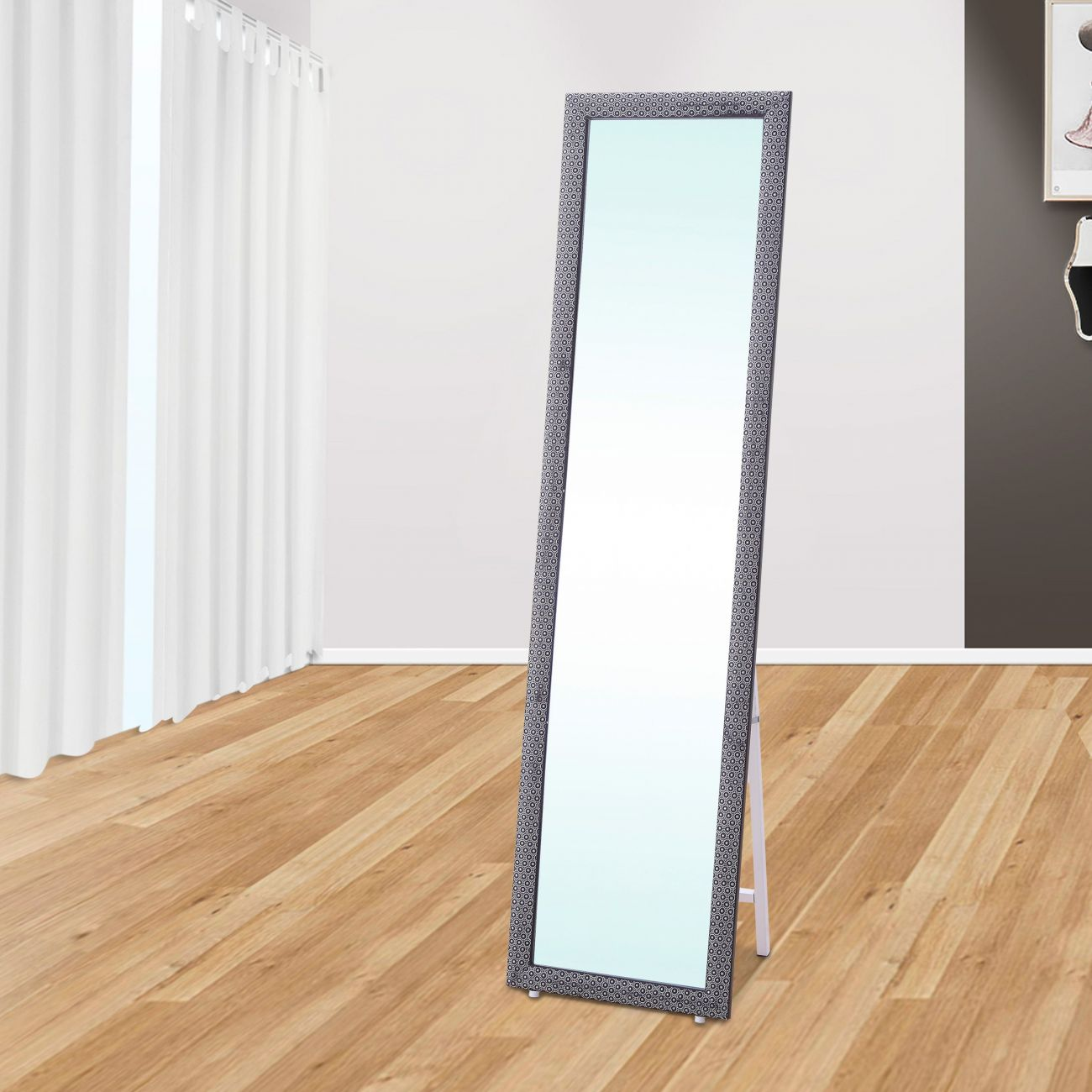 Un espejo alto y rectangular con marco estampado se alza sobre un suelo de madera.