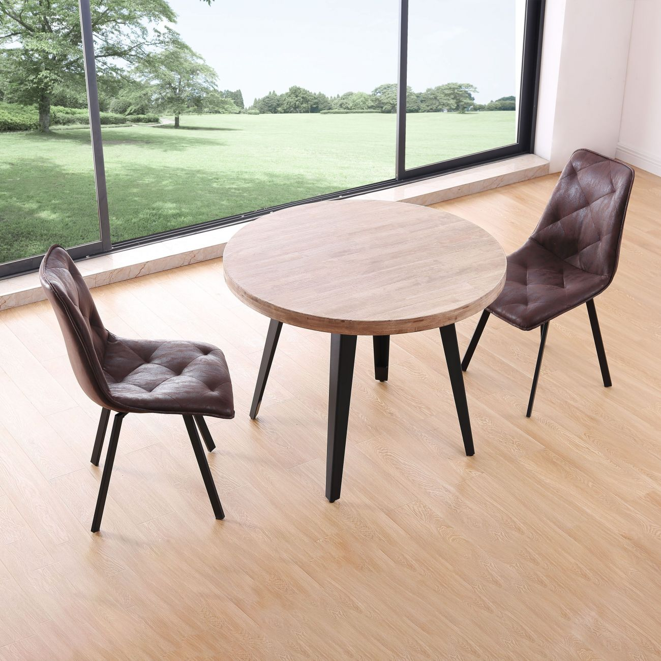 Mesa redonda de madera con dos sillas marrones frente a una gran ventana con vistas a un césped verde.