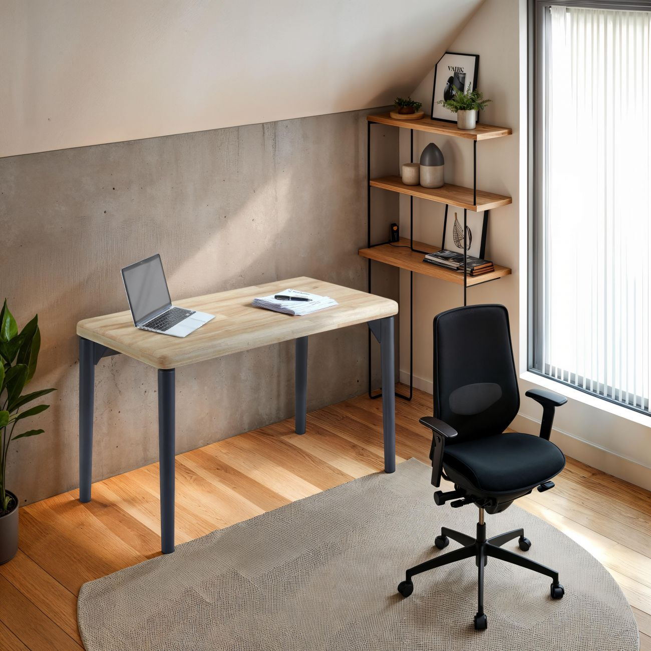 Un escritorio con portátil y silla en una oficina abuhardillada con pared de hormigón y estantería.