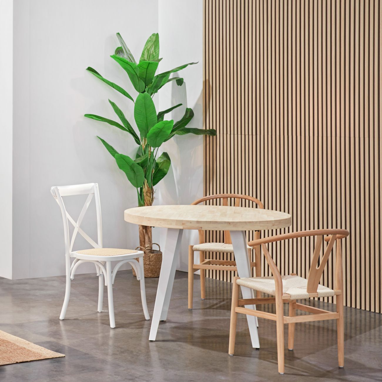 Una mesa redonda de madera con sillas blancas y de madera junto a una planta grande.