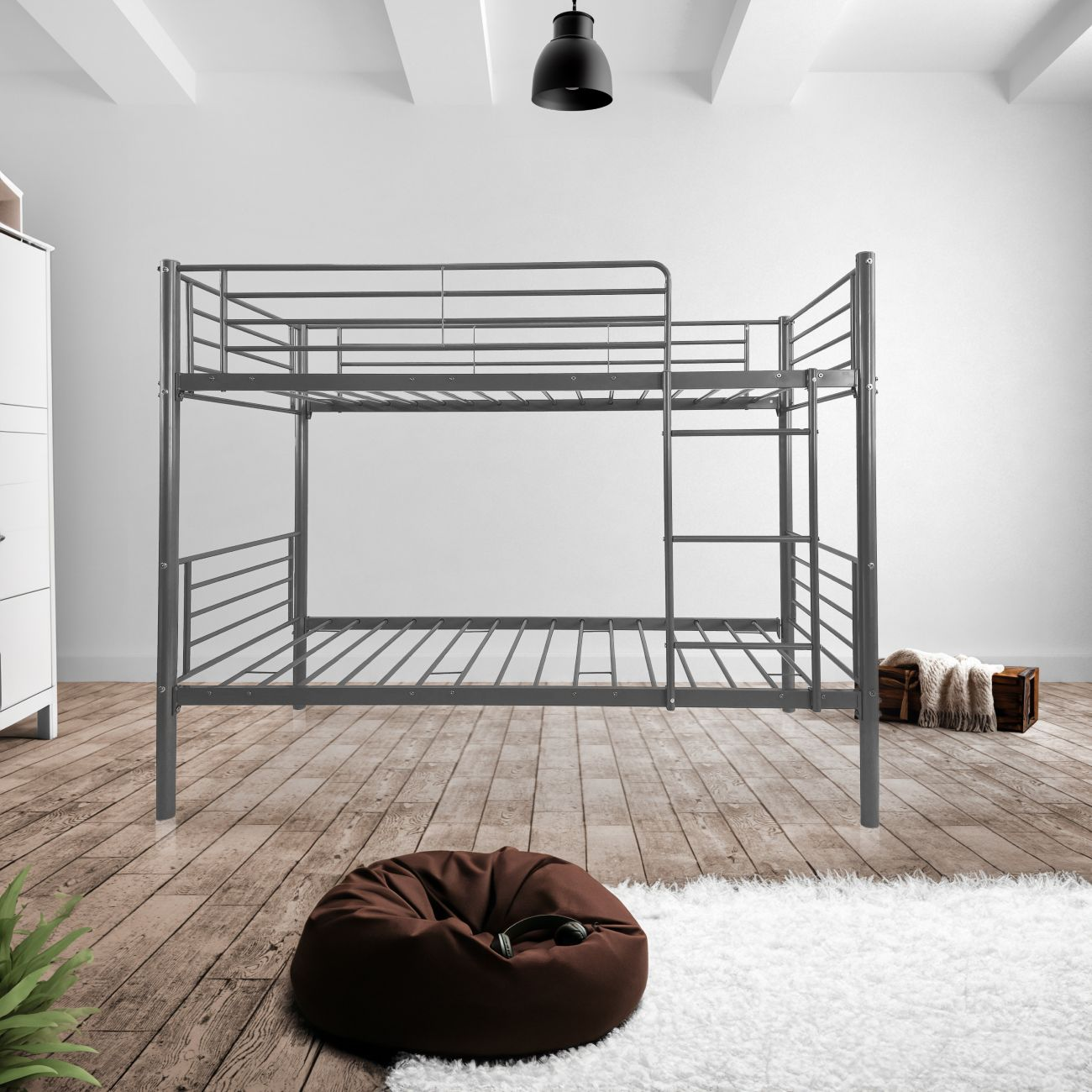 Una litera de metal gris con escalera, un puf marrón y un cofre de madera cerca.