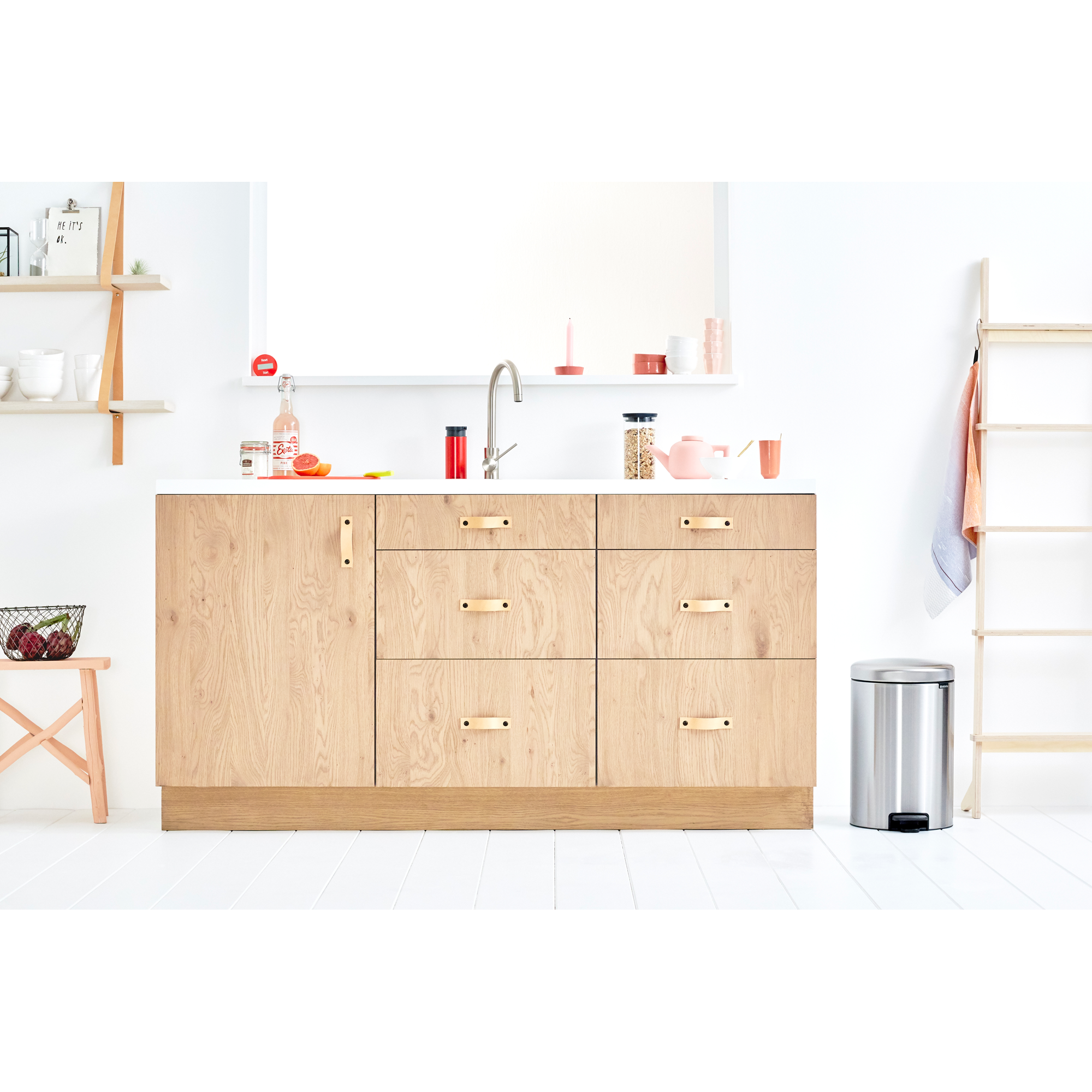 Eine helle Küche mit Holzschränken, einem Wasserhahn, Obst und einem Mülleimer.