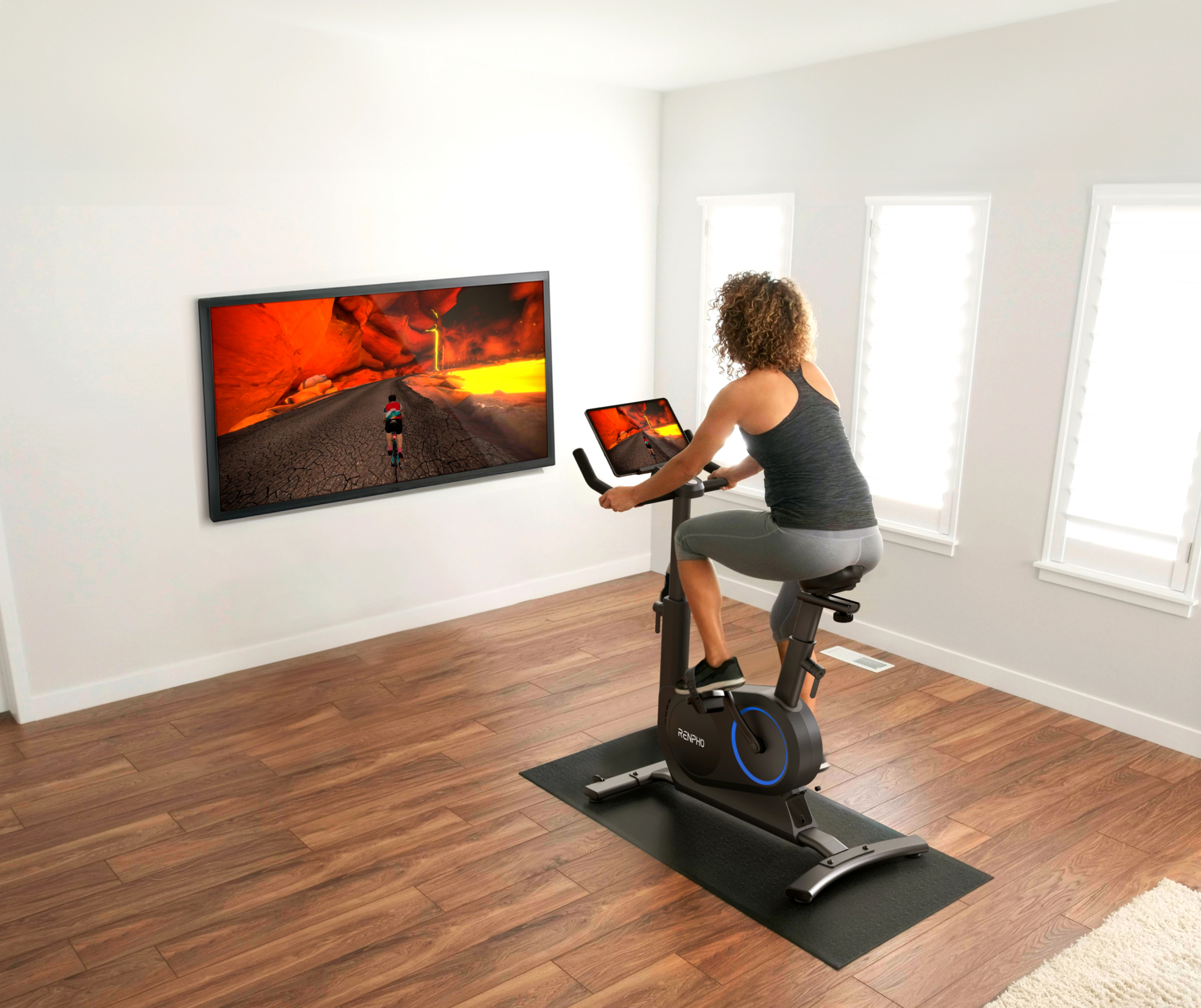 Frau auf Heimtrainer vor großem Bildschirm mit virtueller Landschaft.