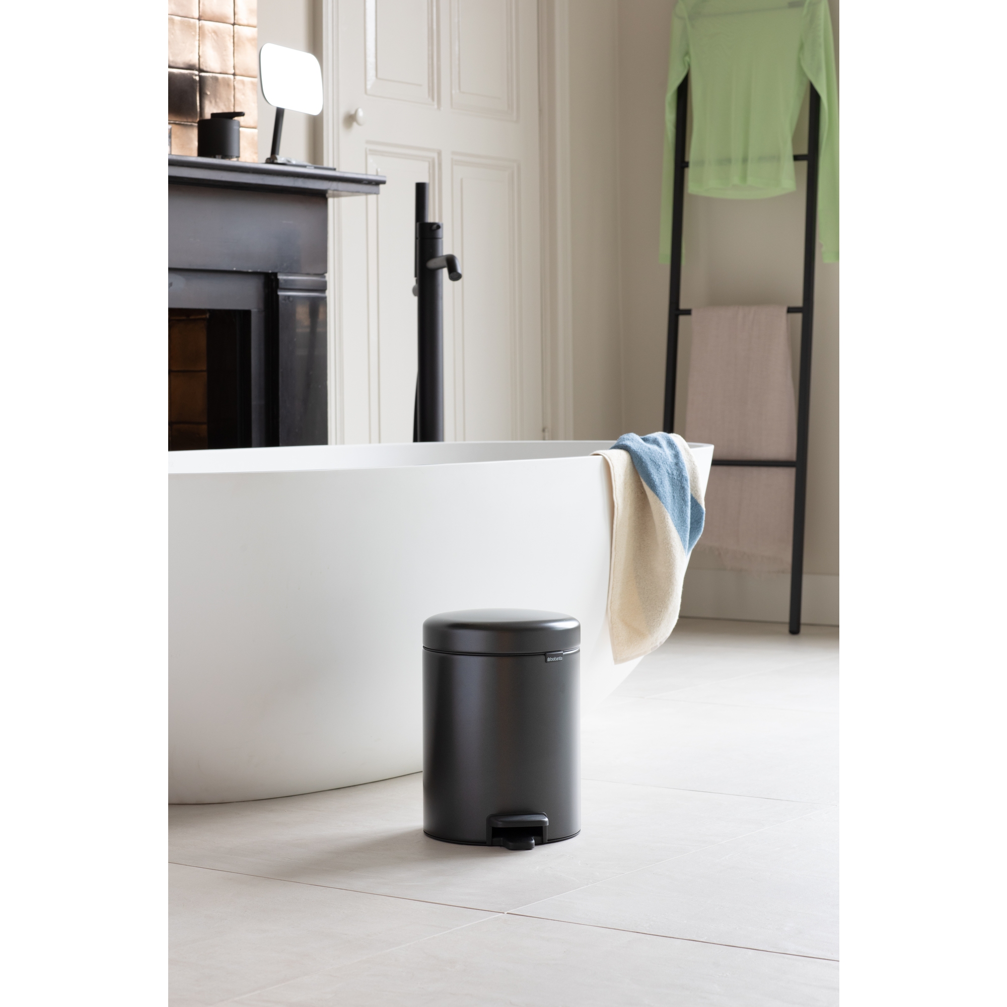 Un cubo de basura negro junto a una bañera blanca con toallas.