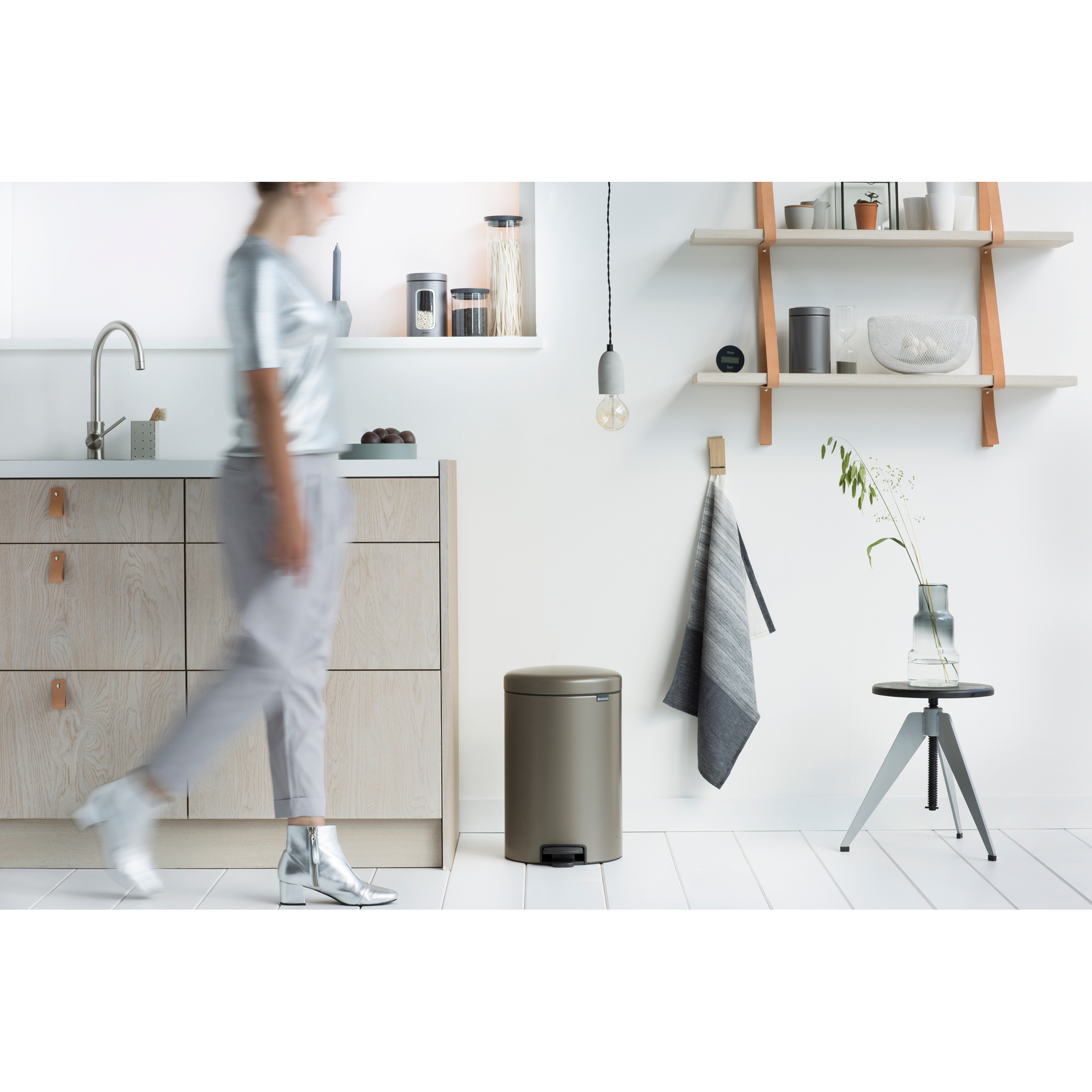 Een vrouw in het zilver loopt langs een keuken met houten kasten en een prullenbak.