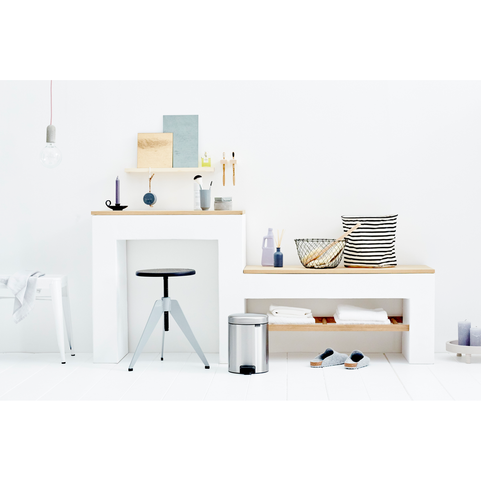 A bathroom scene with a stool, trash can, and folded towels.