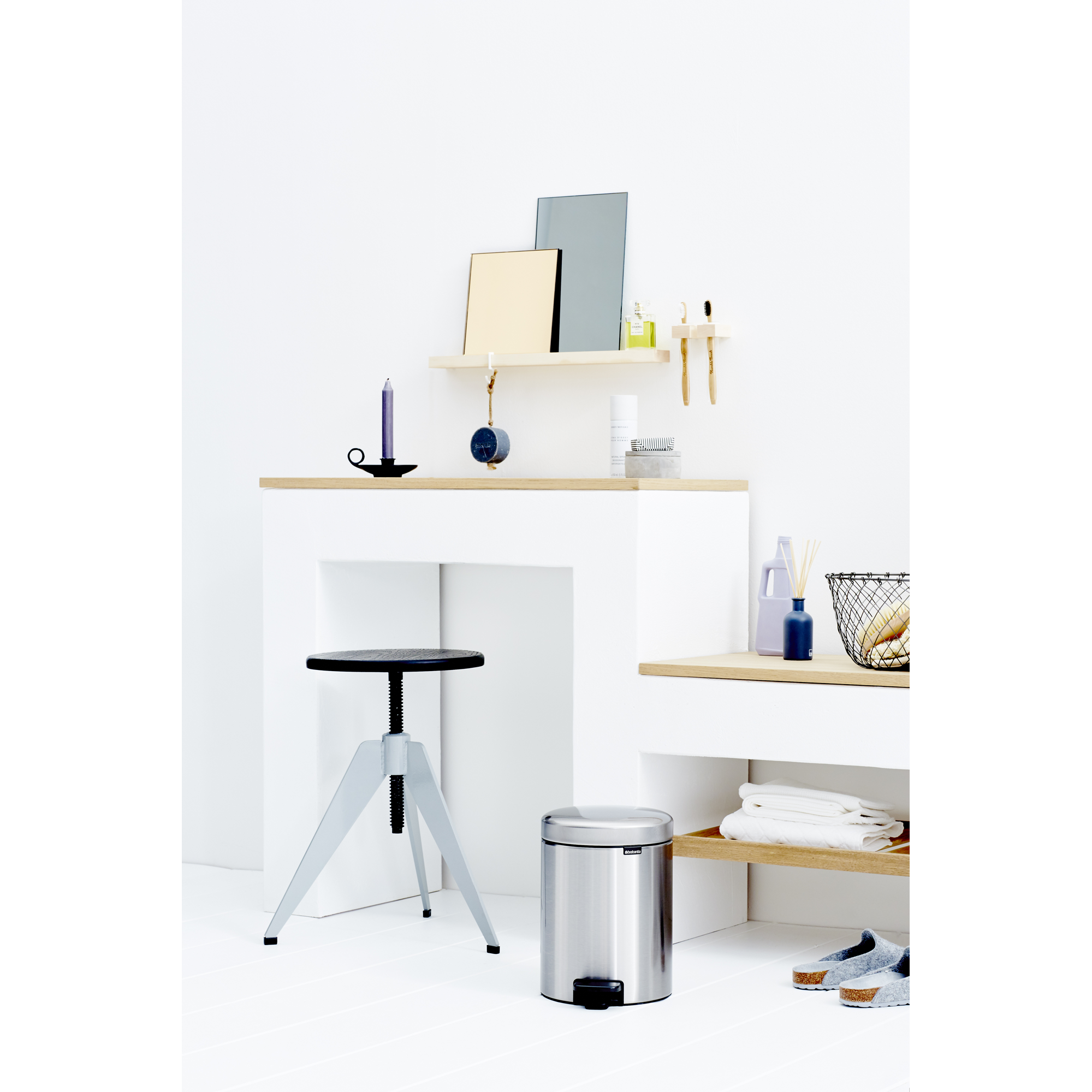 A bright room with a metal stool, a trash can, and shelves holding bathroom items.