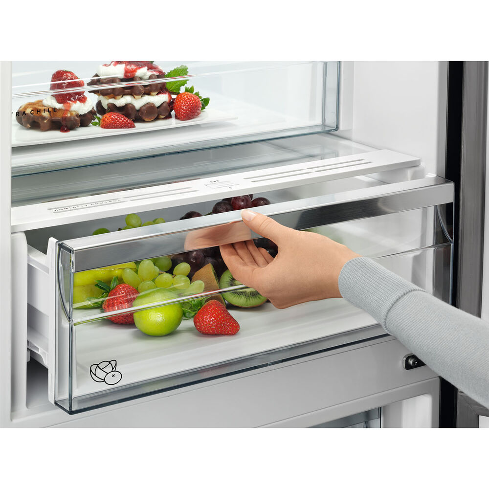 Una mano apre un cassetto pieno di frutta fresca, tra cui uva, fragole e kiwi.