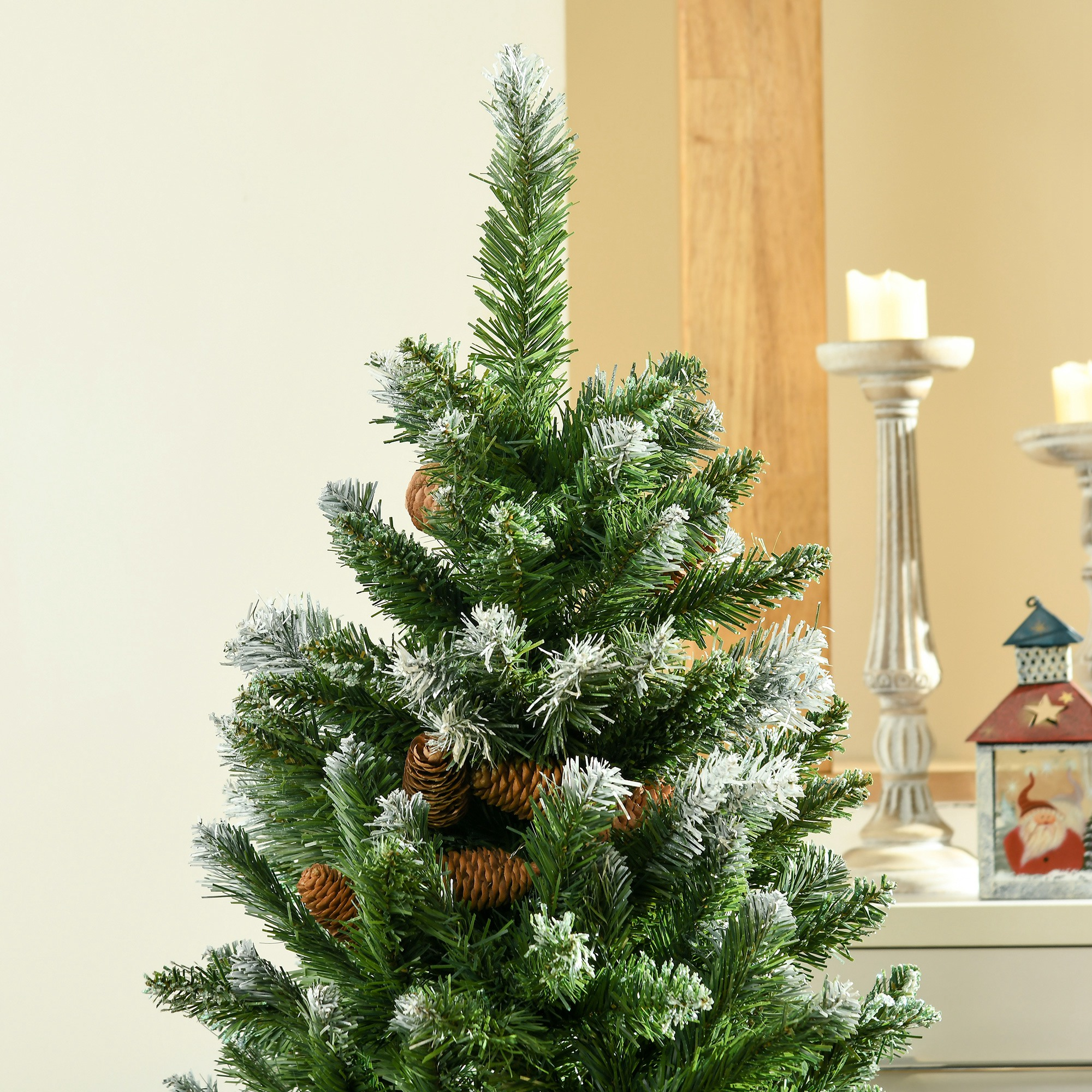 Un árbol de Navidad artificial con piñas y nieve, candelabros y linterna al fondo.