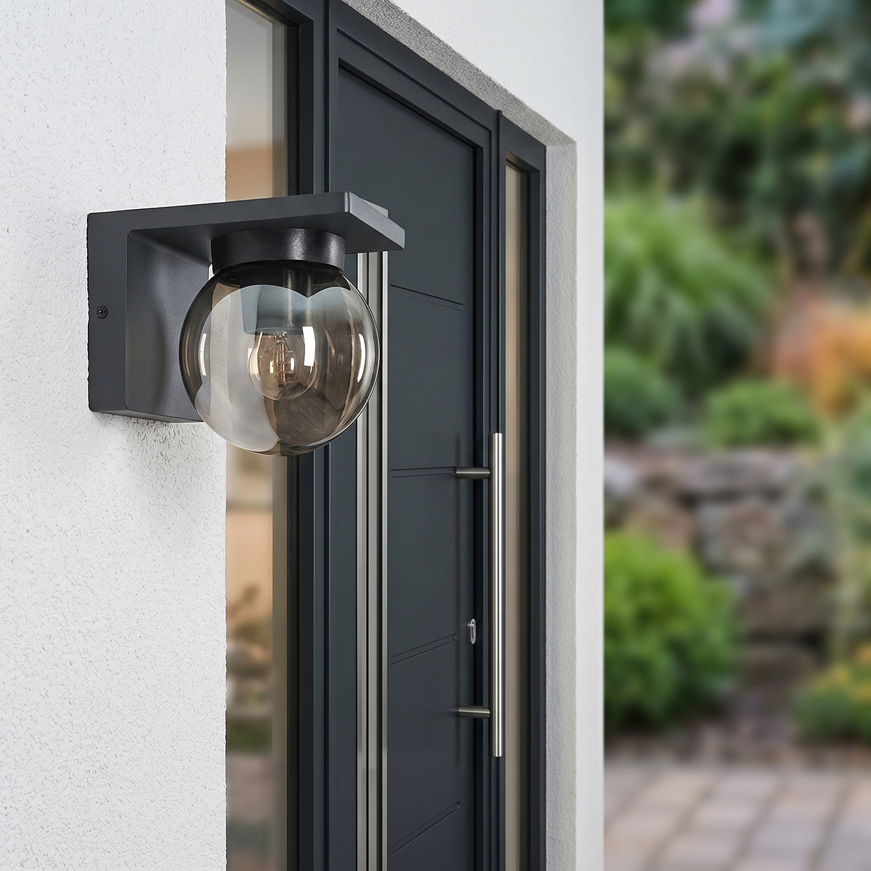 Moderne graue Wandleuchte mit Glaskugel neben einer dunklen Tür.